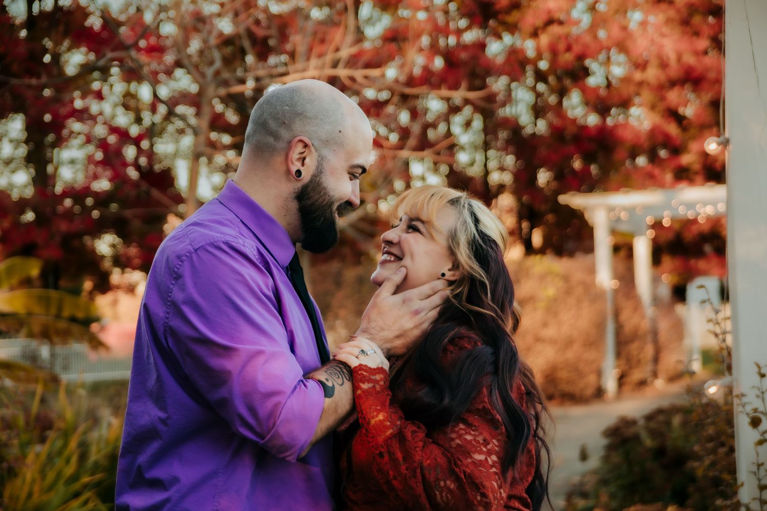 A couple shares a romantic moment outdoors during autumn with red foliage in the background.
