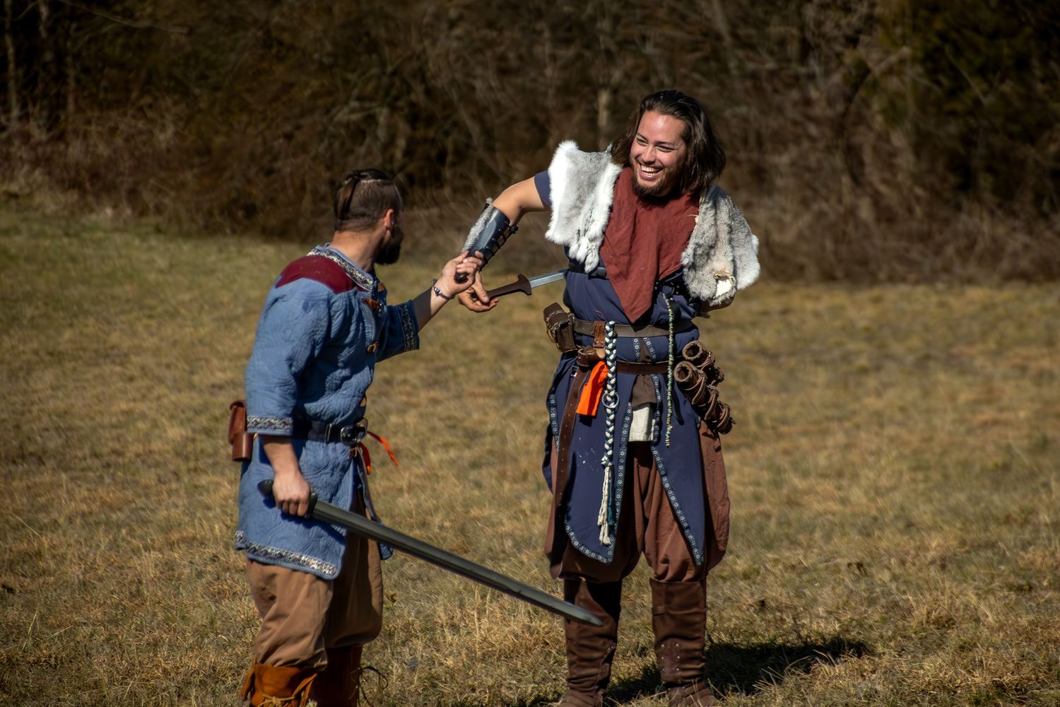 Two medieval costumed fighters sharing a laugh during a historical reenactment in an open field.