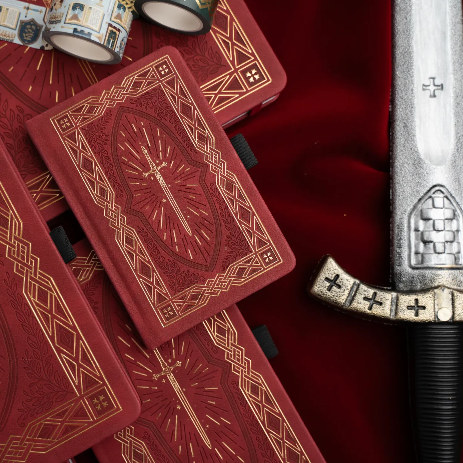 Red playing cards with ornate geometric patterns lie beside a decorative silver sword handle against burgundy velvet.