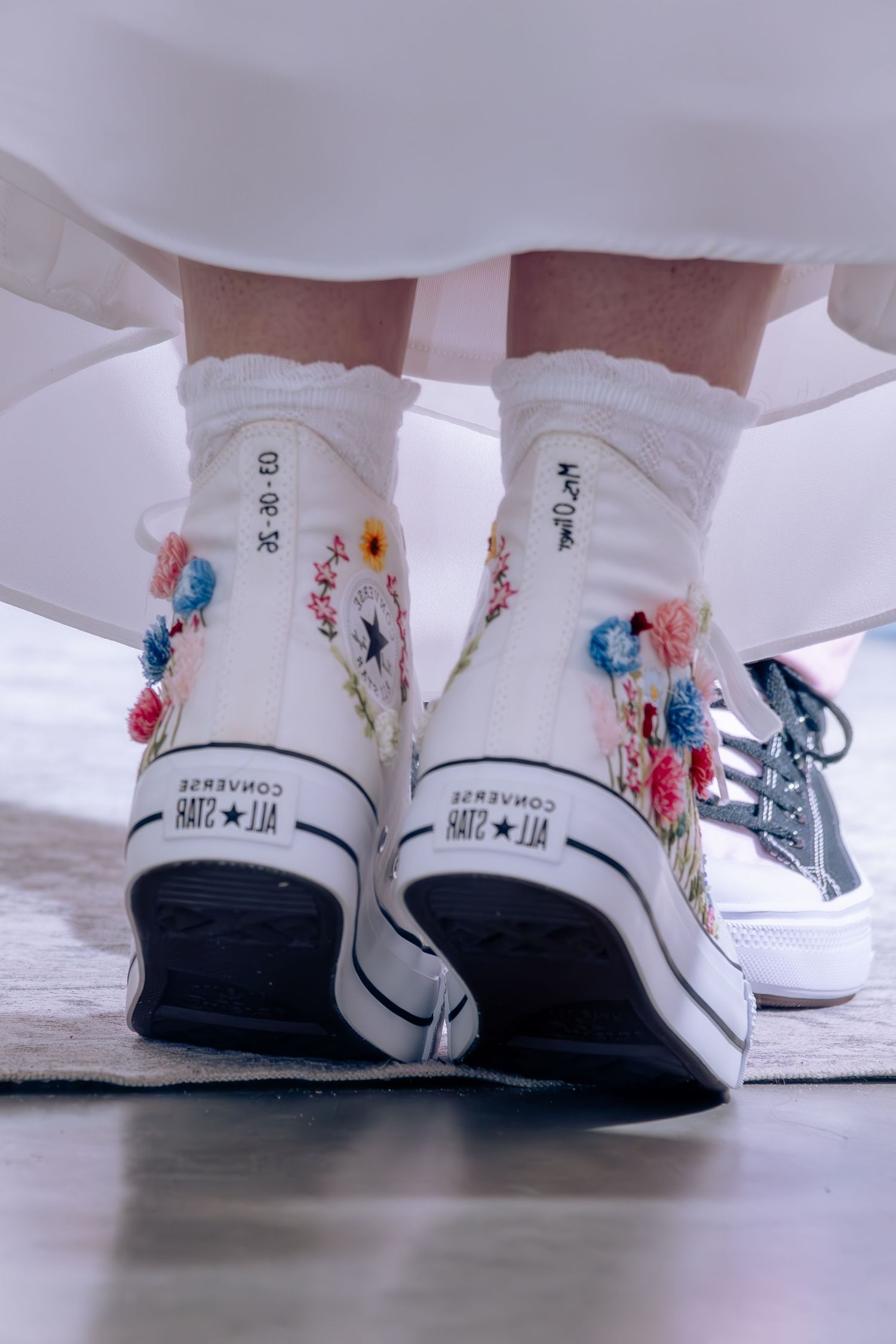 White Converse sneakers decorated with delicate floral embroidery patterns worn with white socks.
