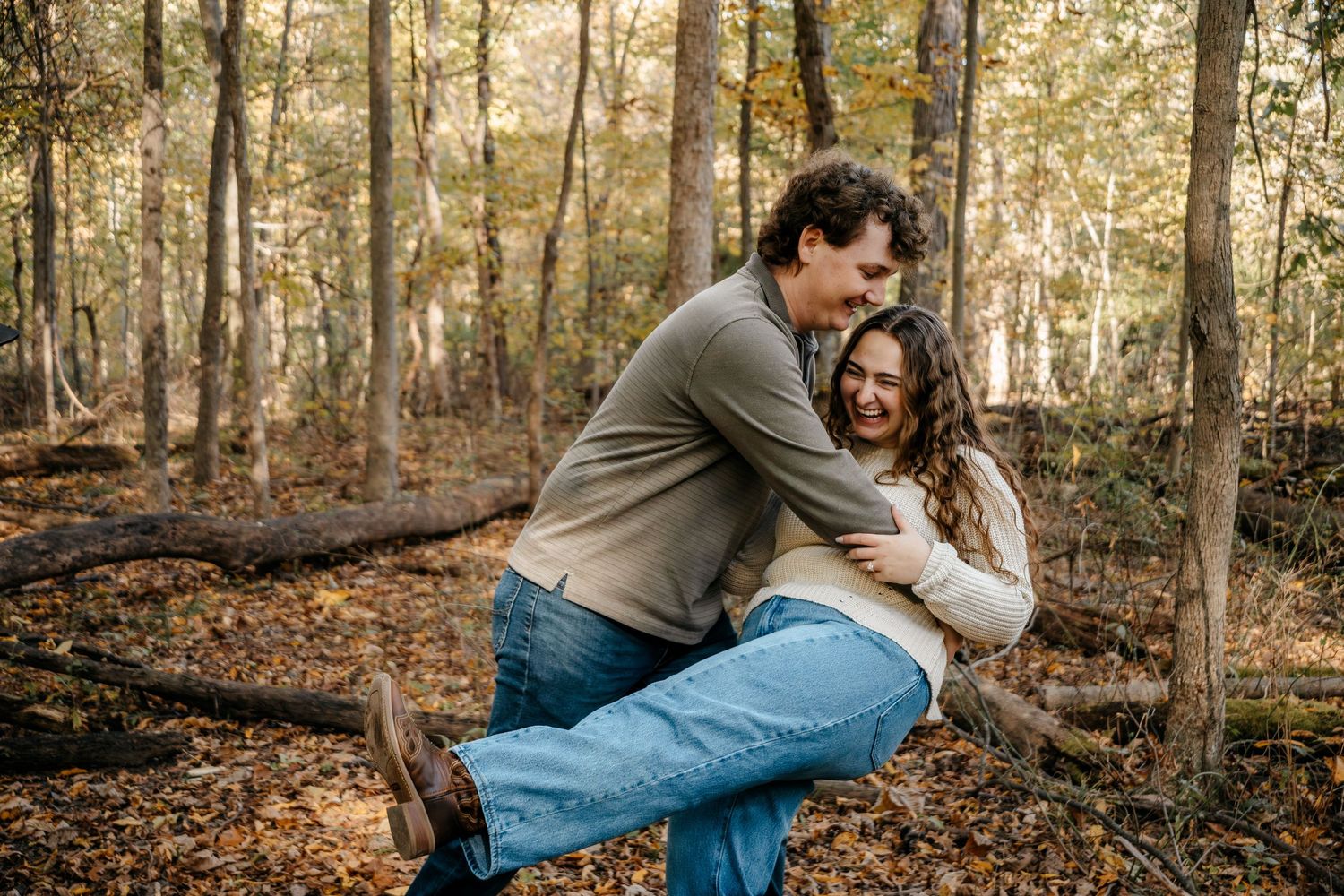 A romantic couple shares intimate moments while posing in a fall forest setting.