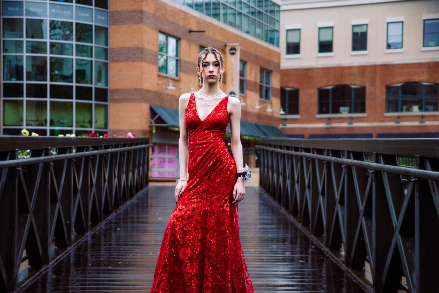 A stunning red formal dress photographed in an urban setting with modern architecture and walkways.