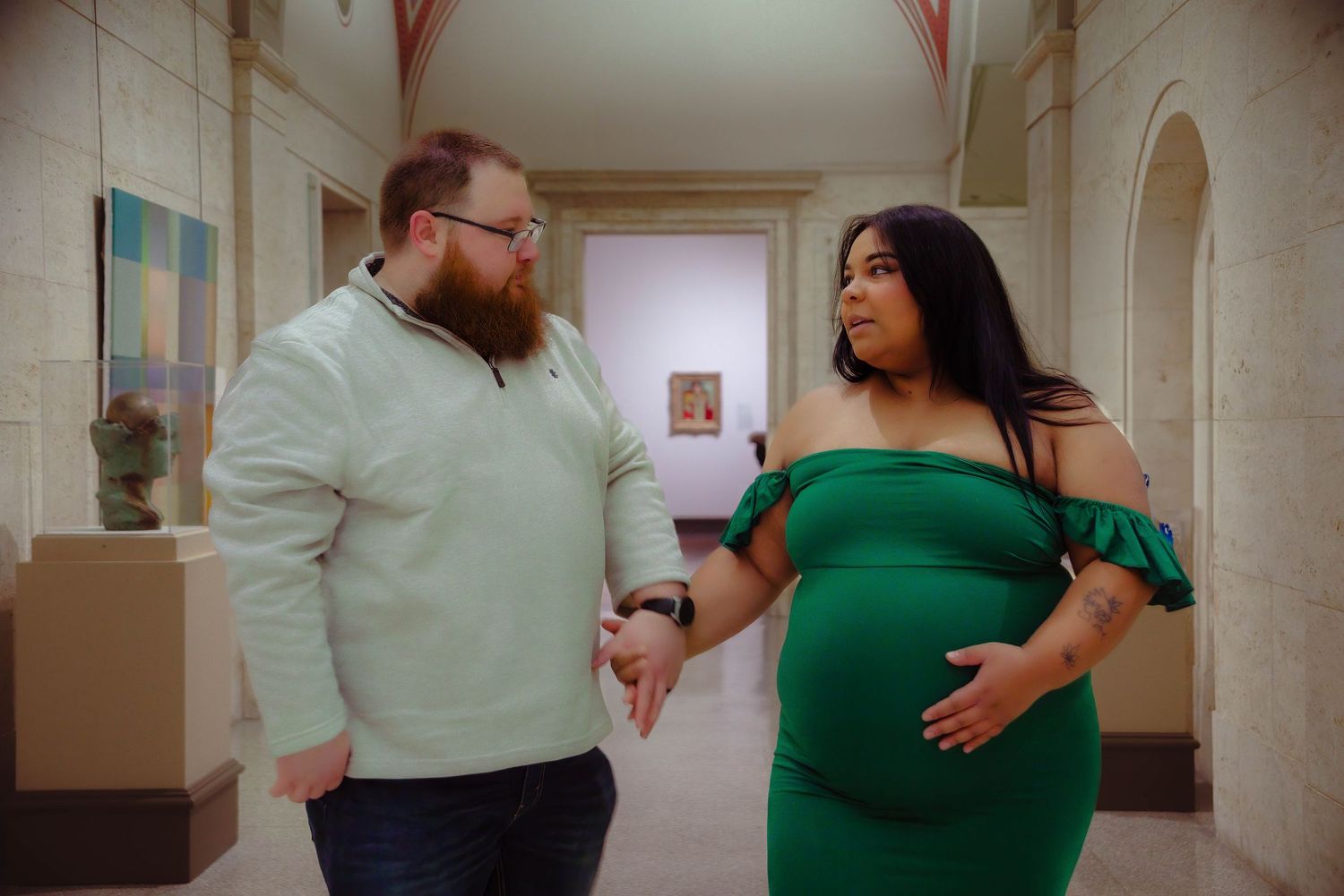 A couple shares a tender moment during their maternity photoshoot in a hallway.