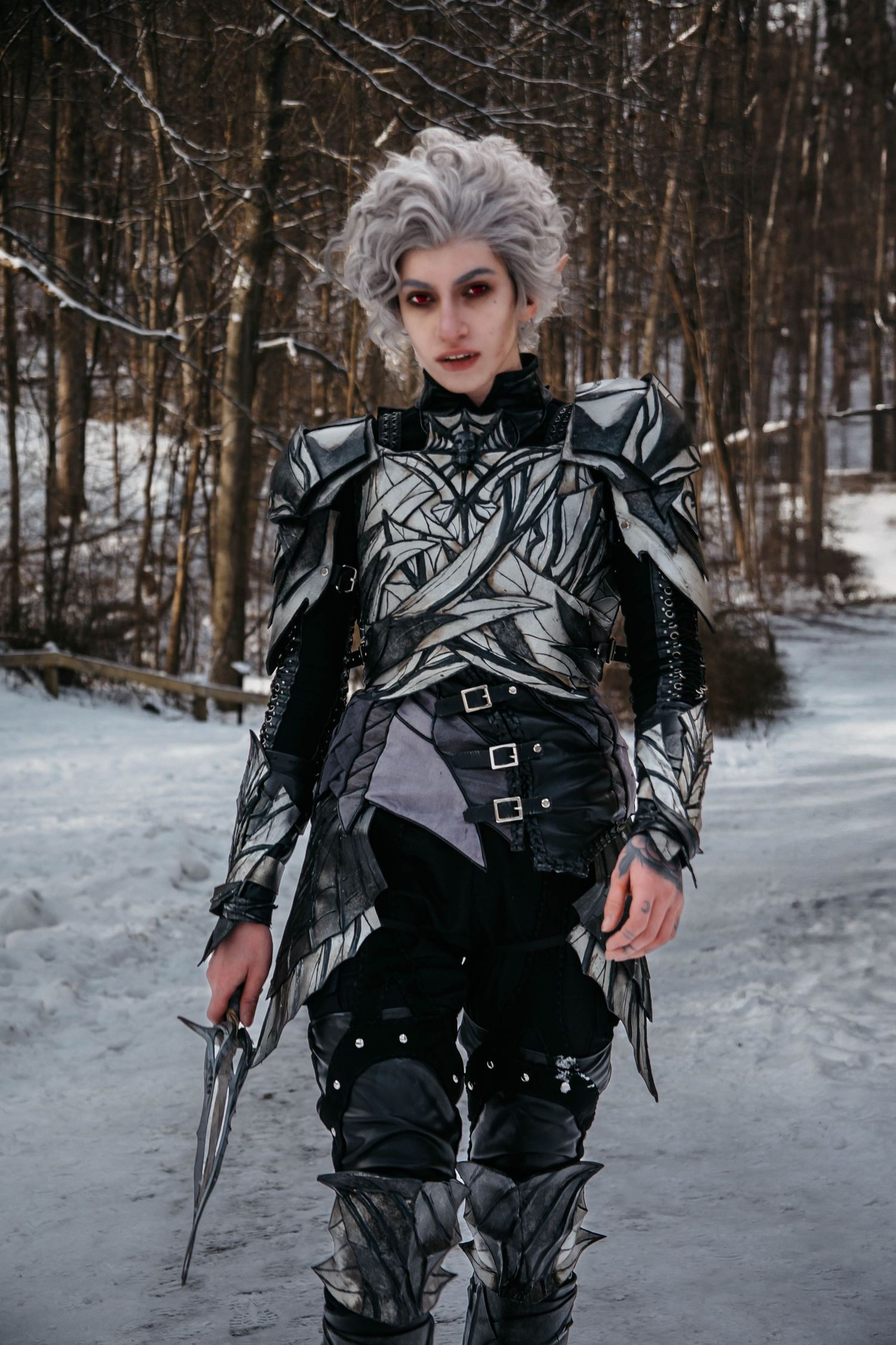 Dark fantasy cosplay outfit with silver armor and black leather details photographed in snowy winter forest setting.