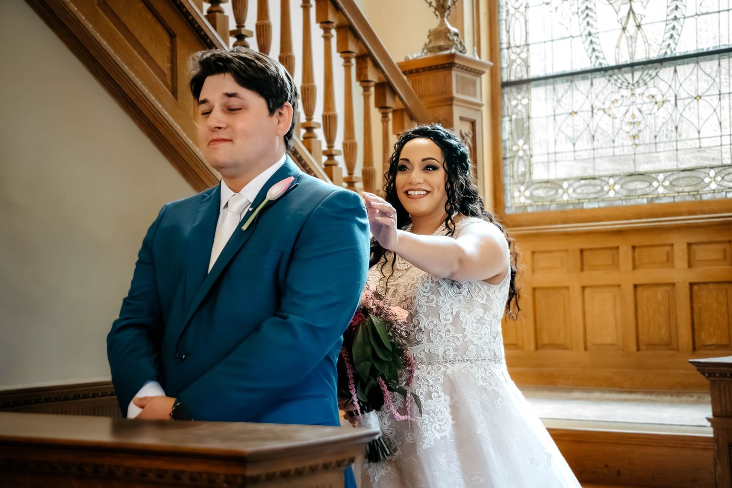 A couple in formal wedding attire stands together in a warmly lit church interior with wooden details.