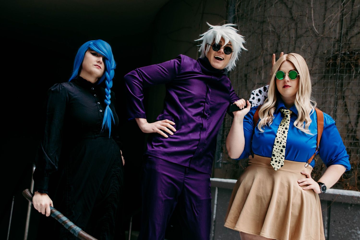 Three cosplayers in anime costumes pose dramatically, featuring blue hair, purple suit, and blue outfit with tie.