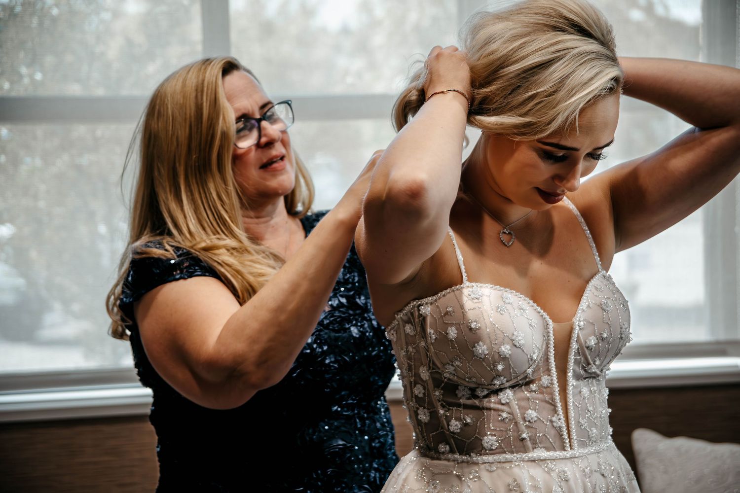 A bridesmaid helps adjust the bride's strapless wedding gown during preparation.