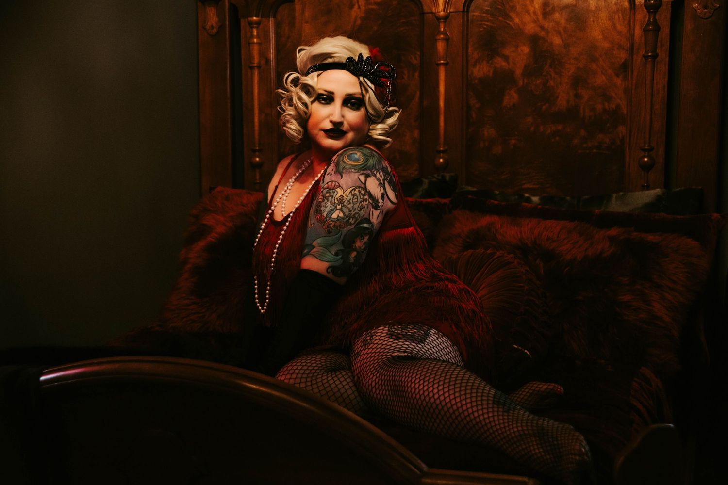 Dramatic vintage-style portrait in dark red lighting with ornate decor and fishnet details.