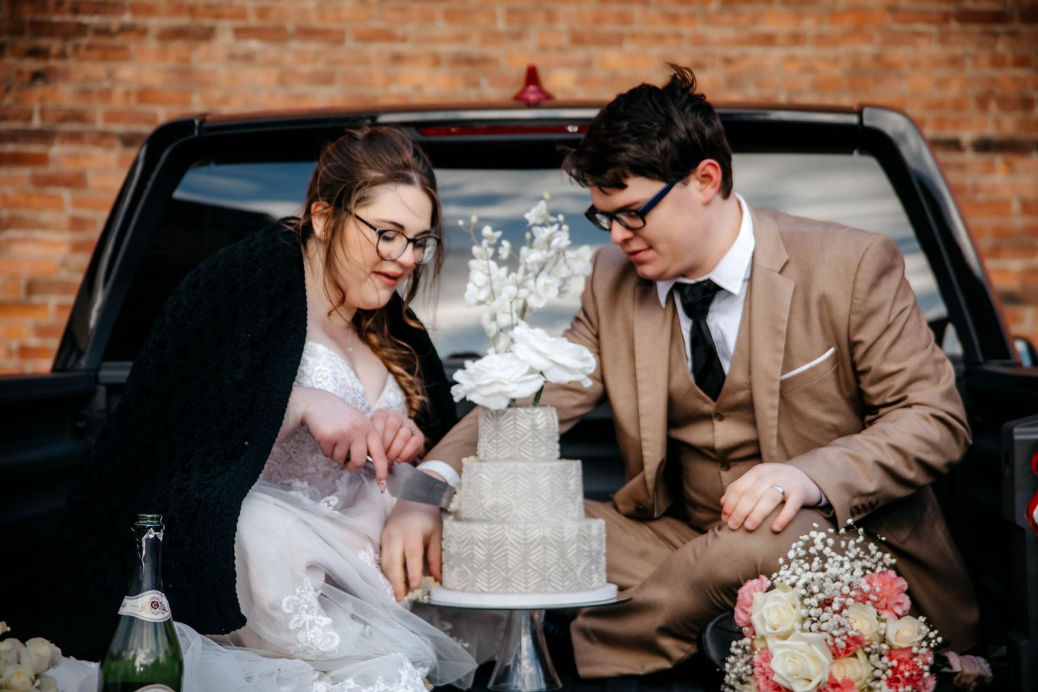 Couple sharing a romantic moment with wedding cake at rustic brick venue with floral decor.