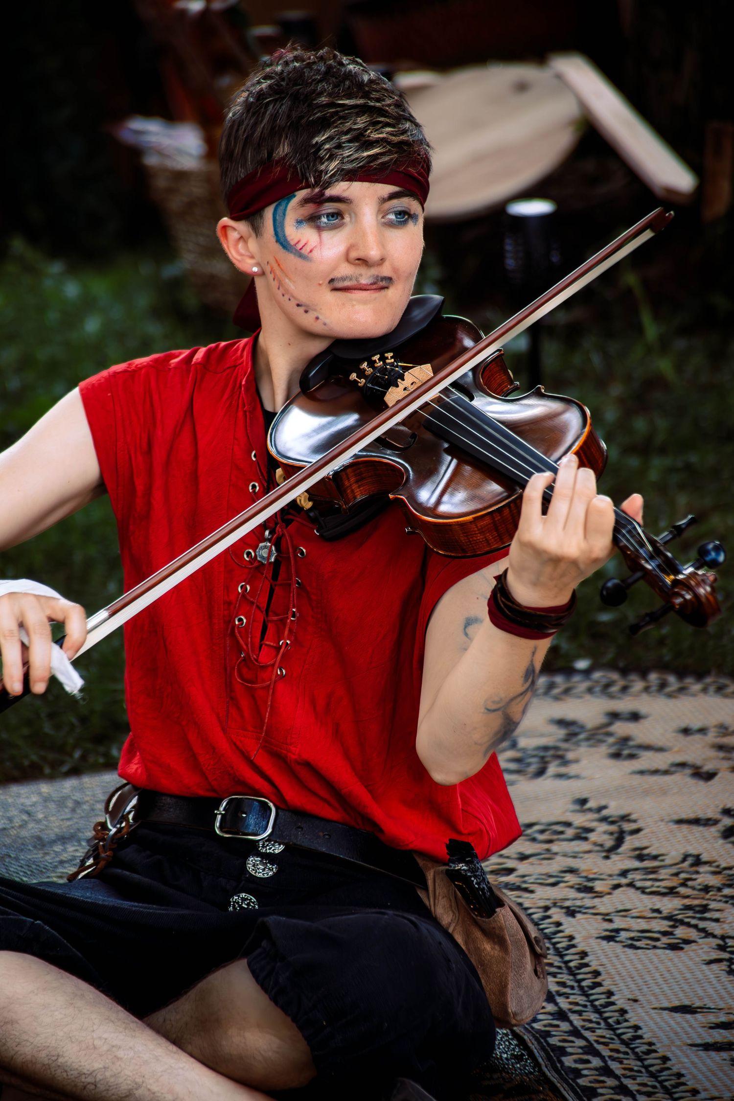 A violinist in a red shirt performs outdoors while sitting on a patterned surface in a series of dynamic poses.
