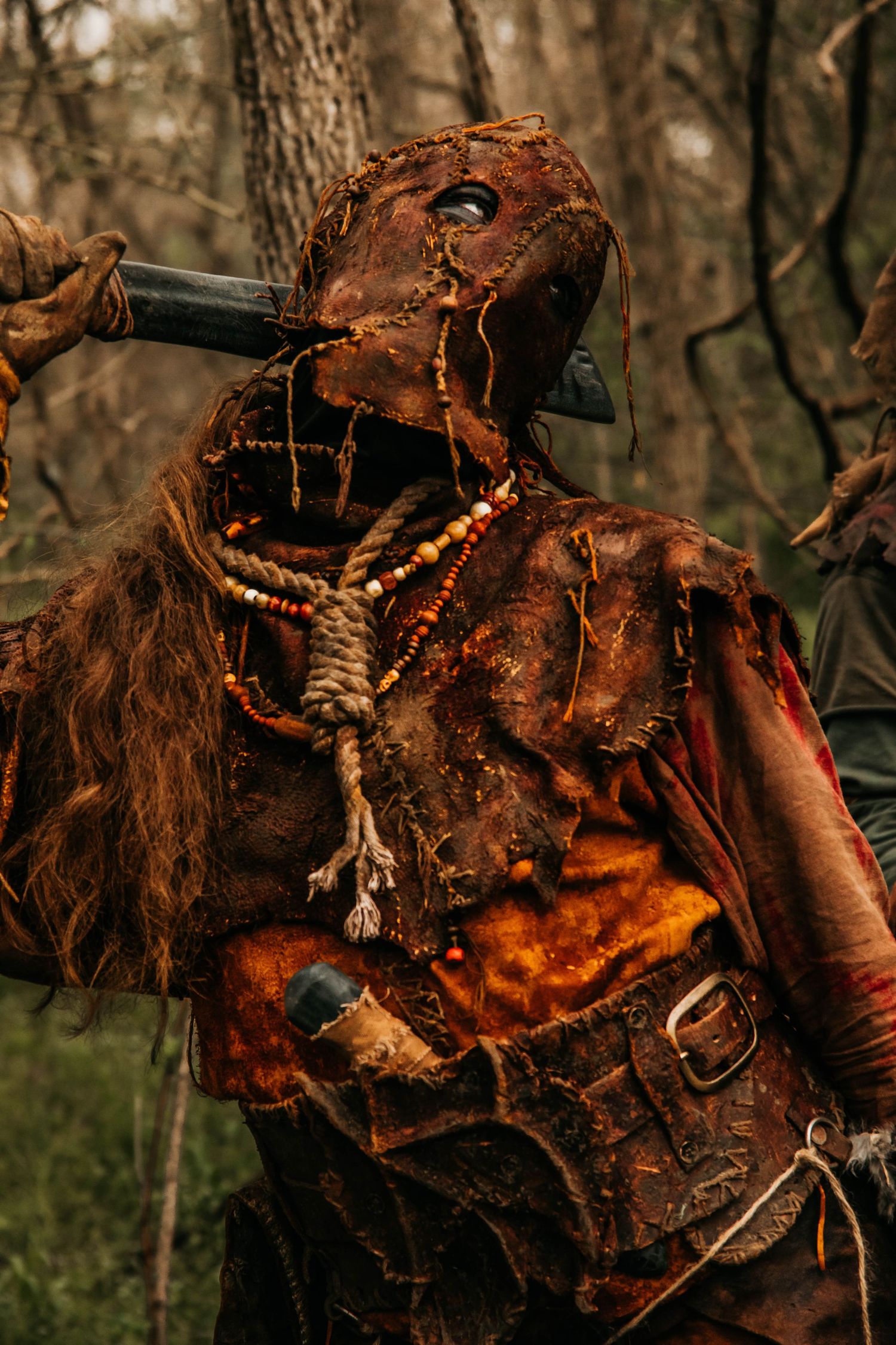 Detailed closeup of weathered leather mask with bone and feather decorations in forest setting.