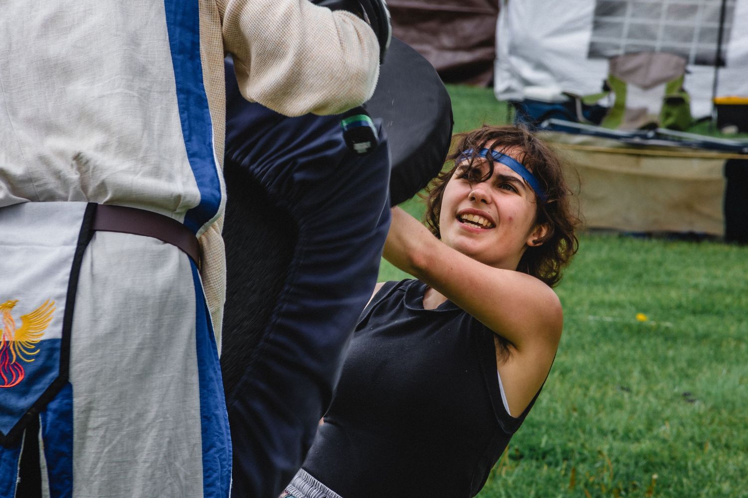 Young woman in medieval costume smiling outdoors at a Renaissance fair event on green grass.