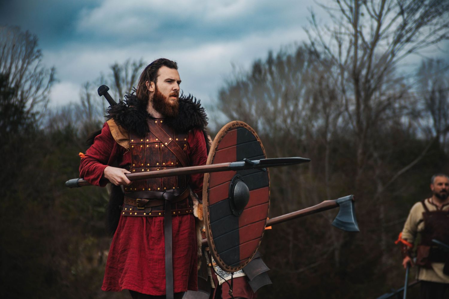 A medieval warrior in red garments holds a sword during an outdoor battle reenactment performance.
