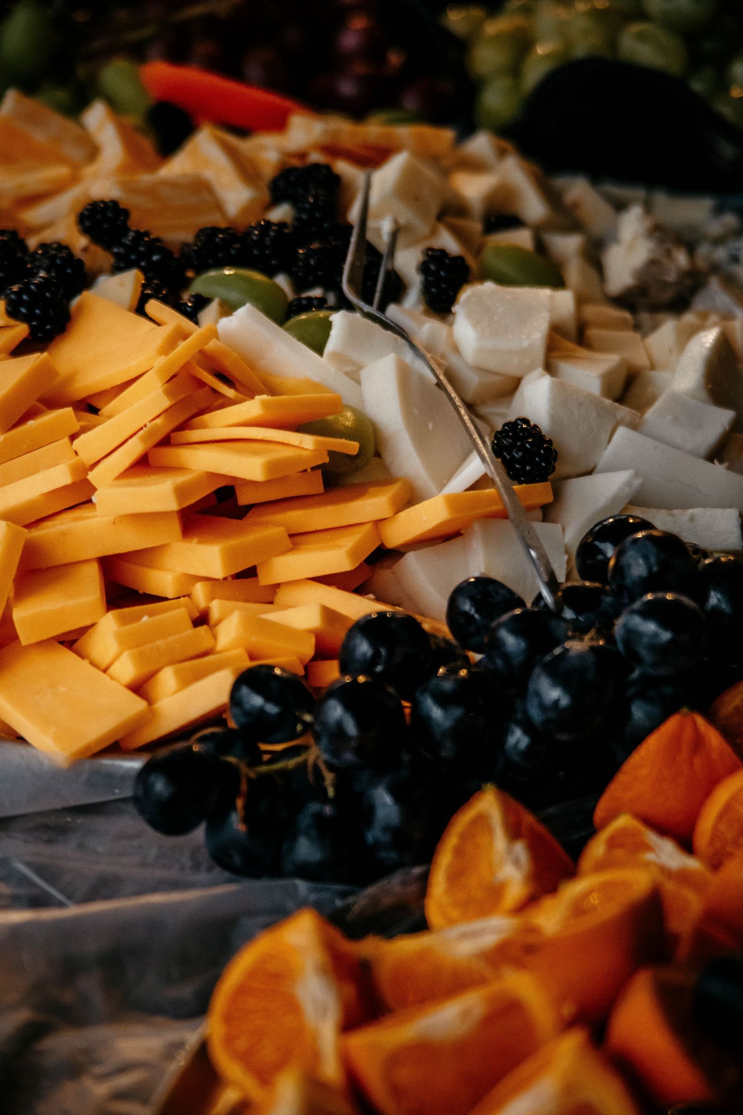 A close-up view of a cheese and fruit platter with cheddar slices, white cheese cubes, and fresh dark grapes.