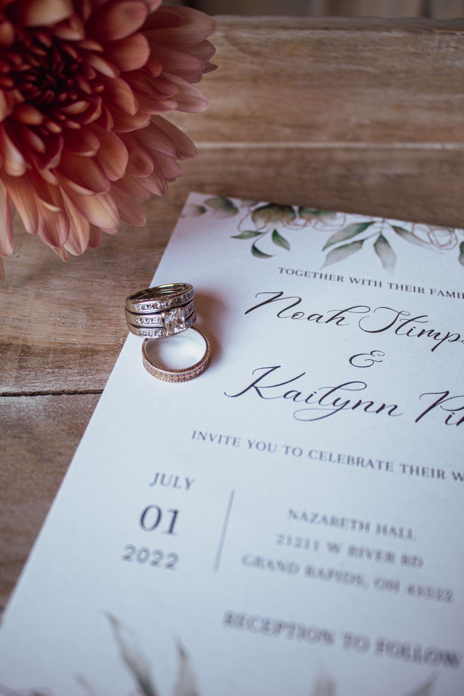 Wedding rings resting on an elegant invitation for Noah and Kailynn, dated July 1, 2022, at Nazareth Hall, Grand Rapids.