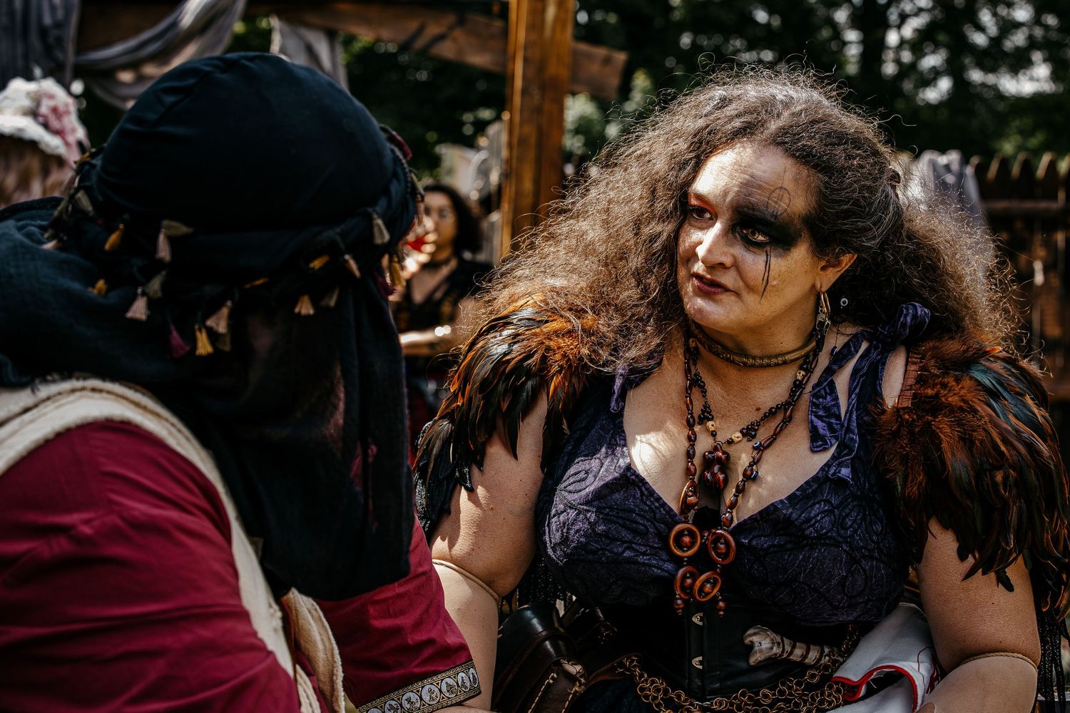 Two costumed performers in dark fantasy attire converse at a Renaissance faire outdoor event.