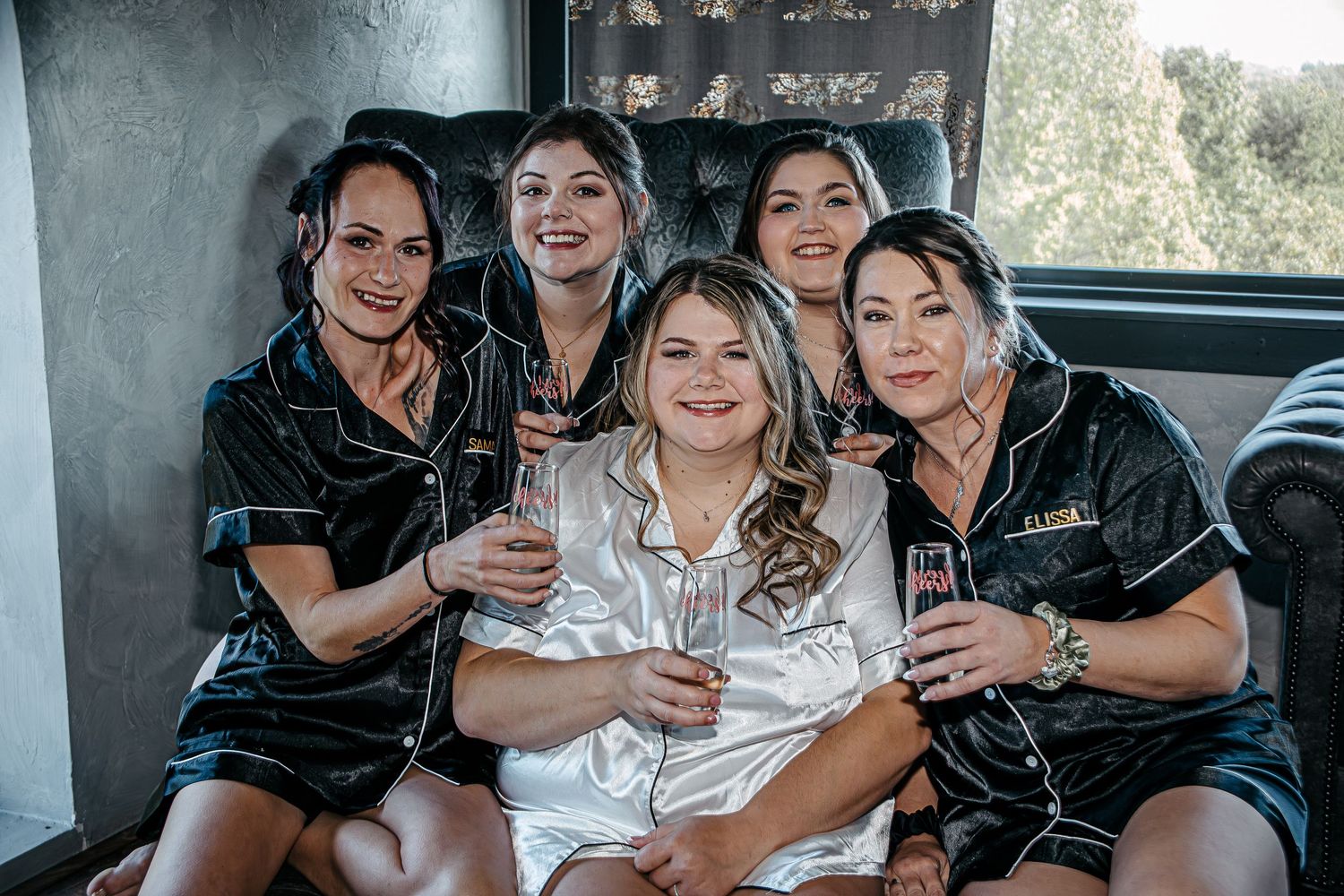 Wedding party in matching black satin robes celebrating with champagne.