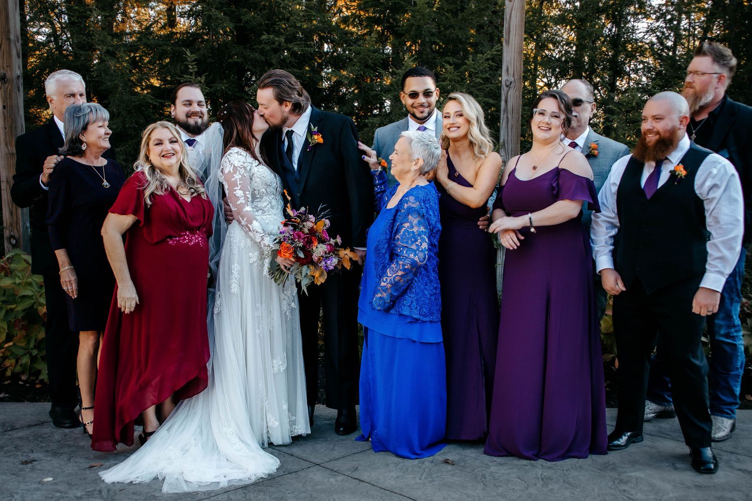 Wedding party in coordinated formal attire featuring burgundy, blue and purple dresses standing together outdoors.