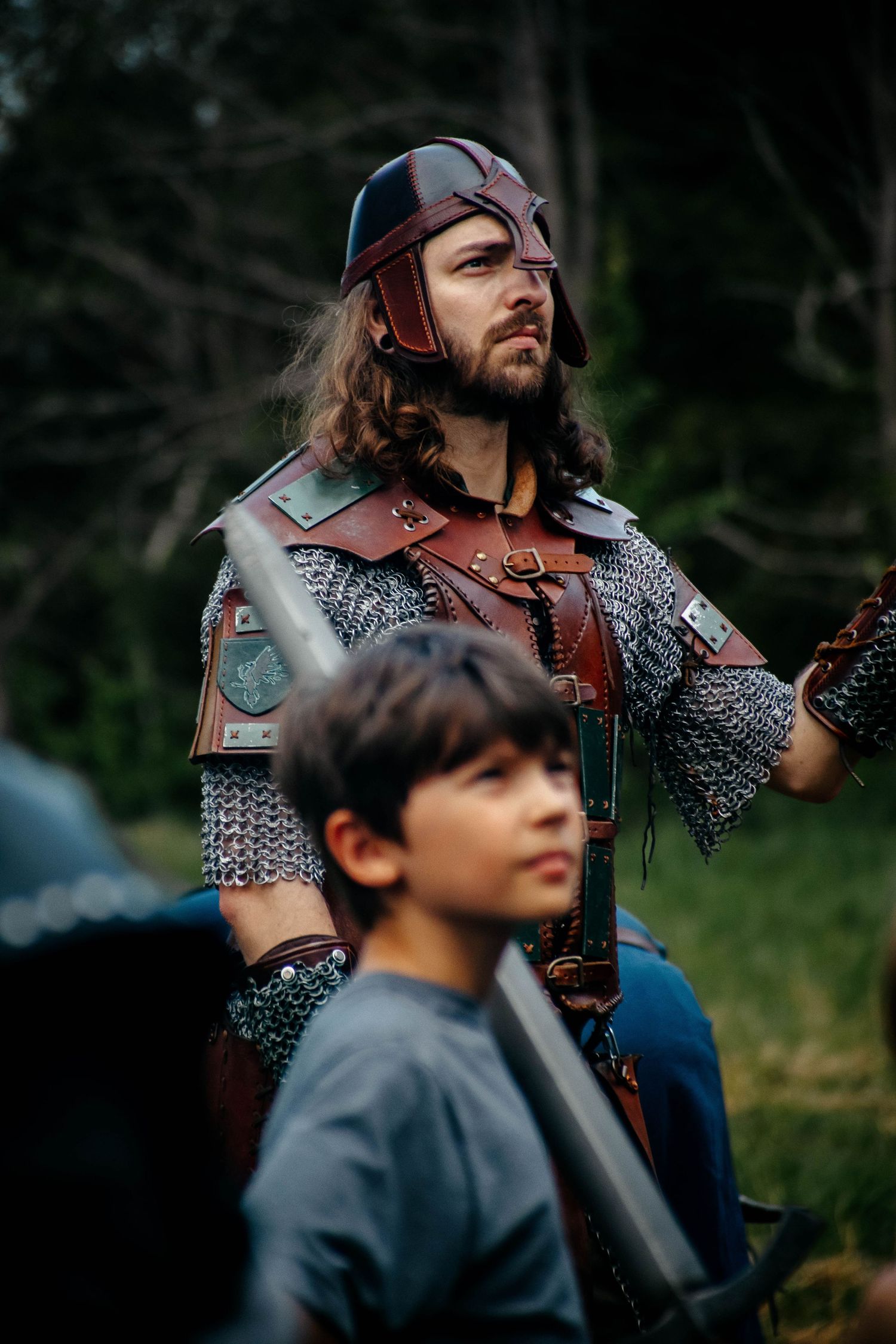 Medieval reenactors wearing chainmail armor and leather gear stand together outdoors.