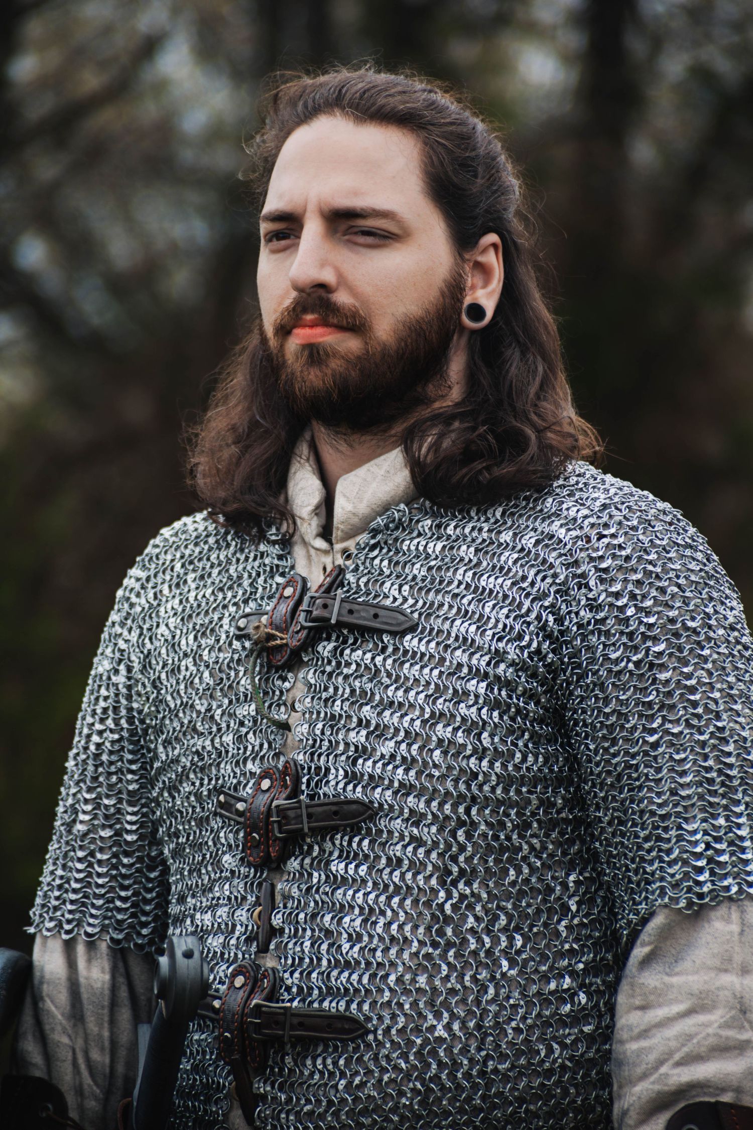 A reenactor wears detailed chainmail armor and leather accessories at a medieval event.