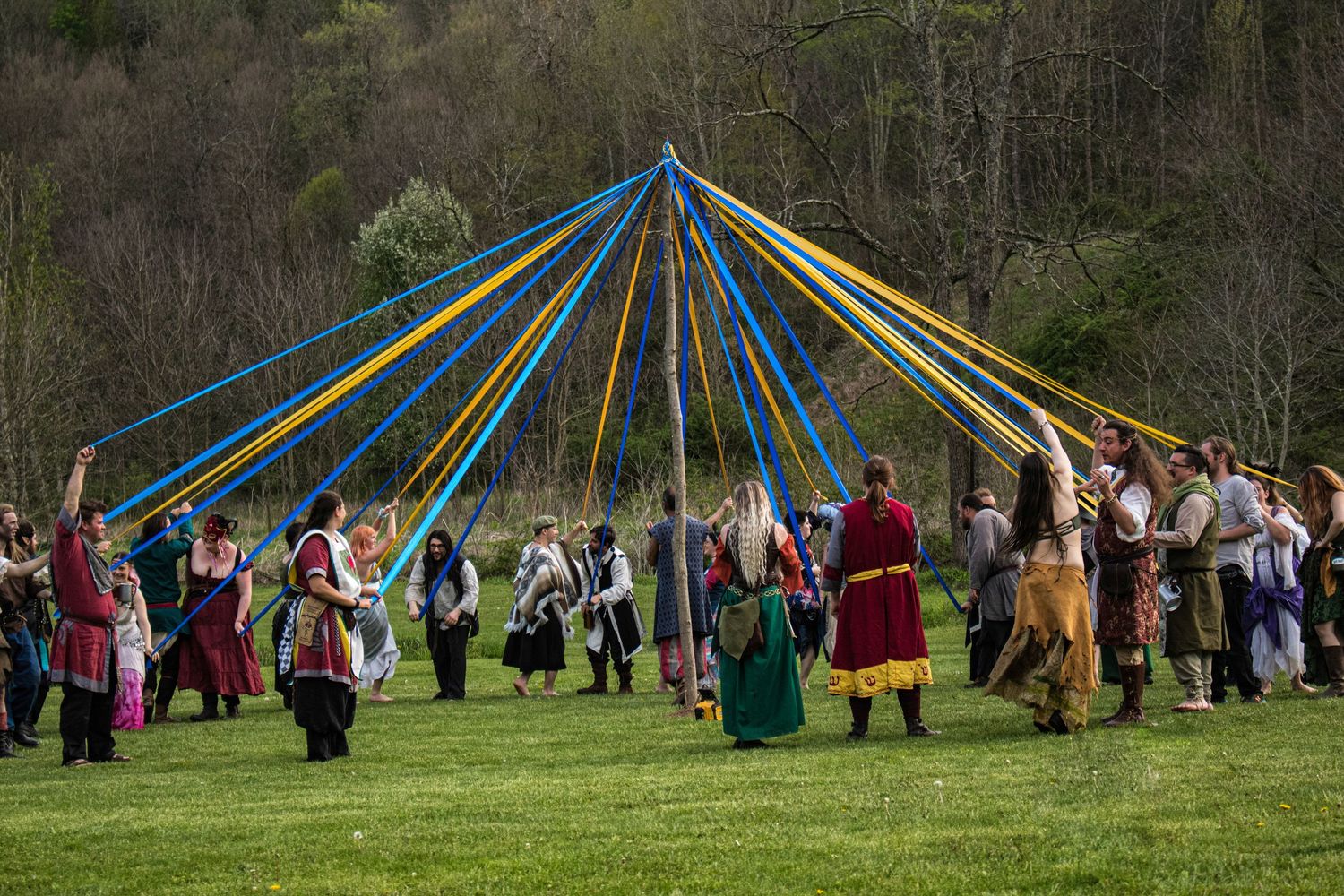 People gather around a traditional maypole with colorful ribbons during a springtime festival celebration.