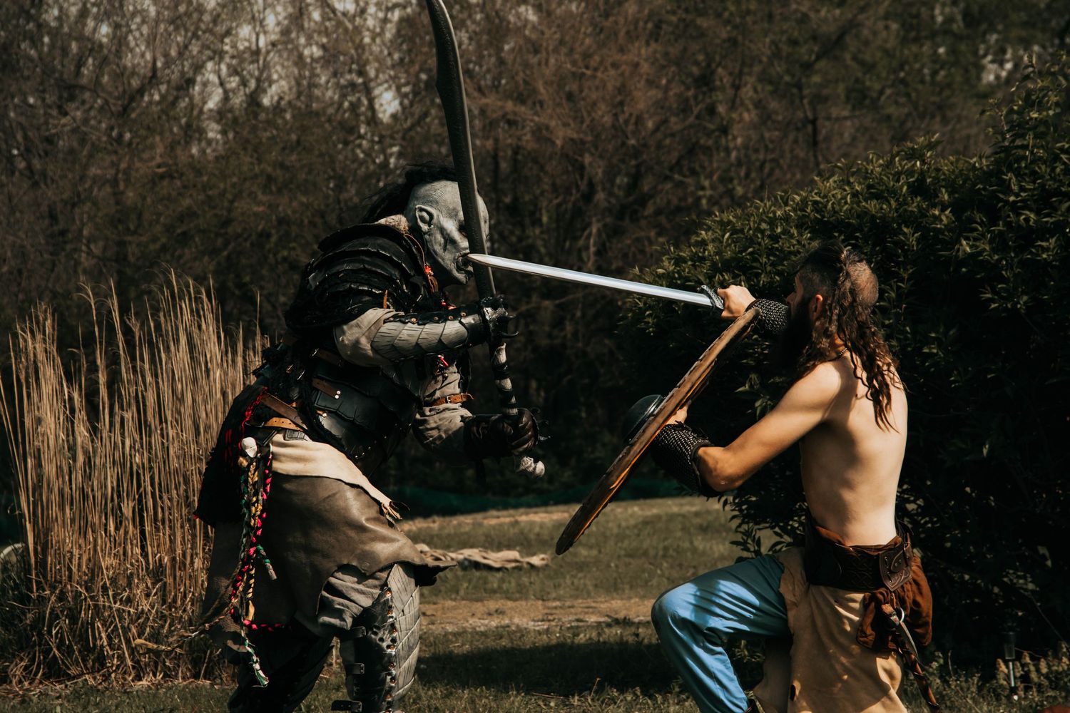 Two people practice martial arts moves in a park with bare trees in the background.