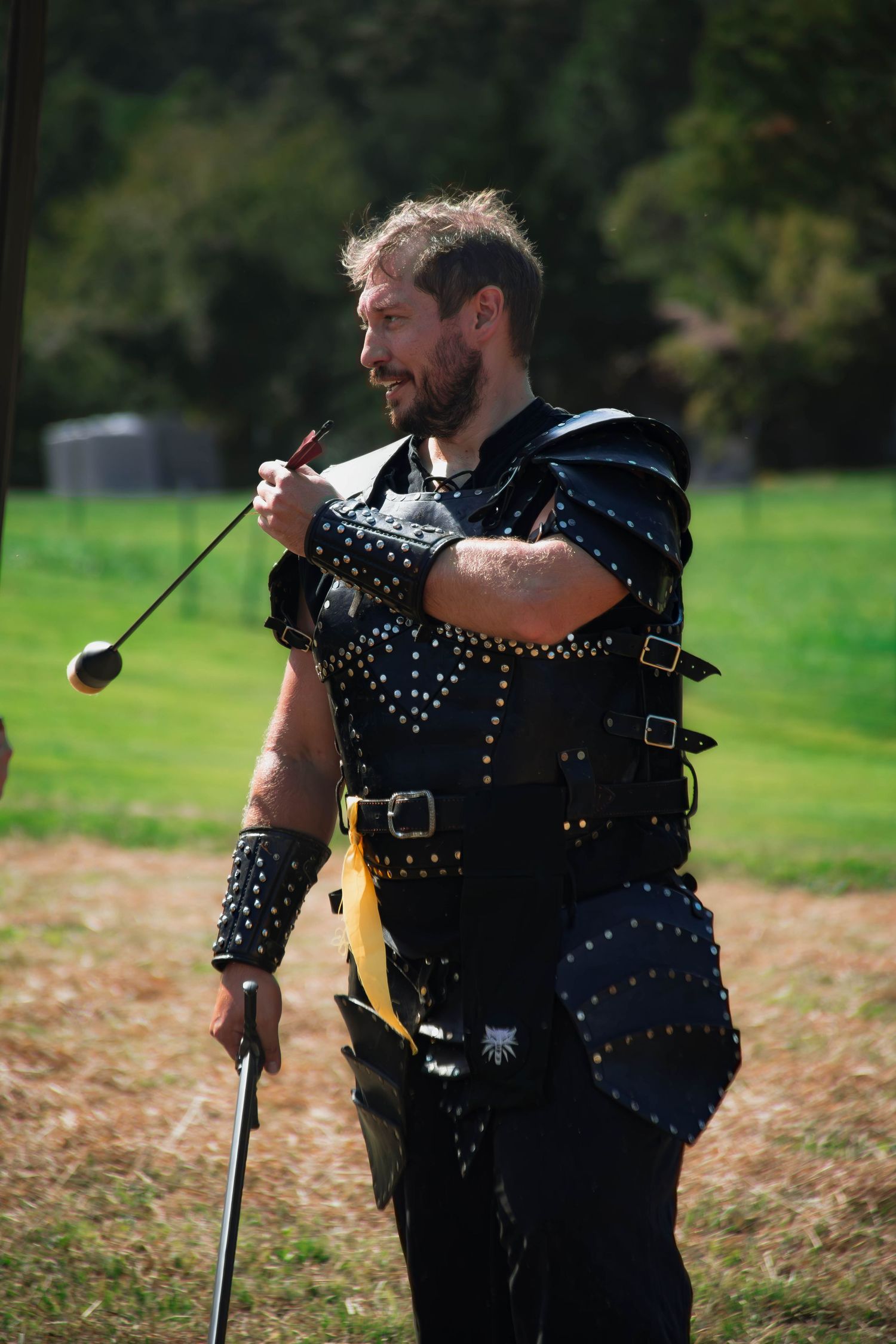 Two people in medieval style leather armor and studded costumes stand together in a grassy outdoor setting.