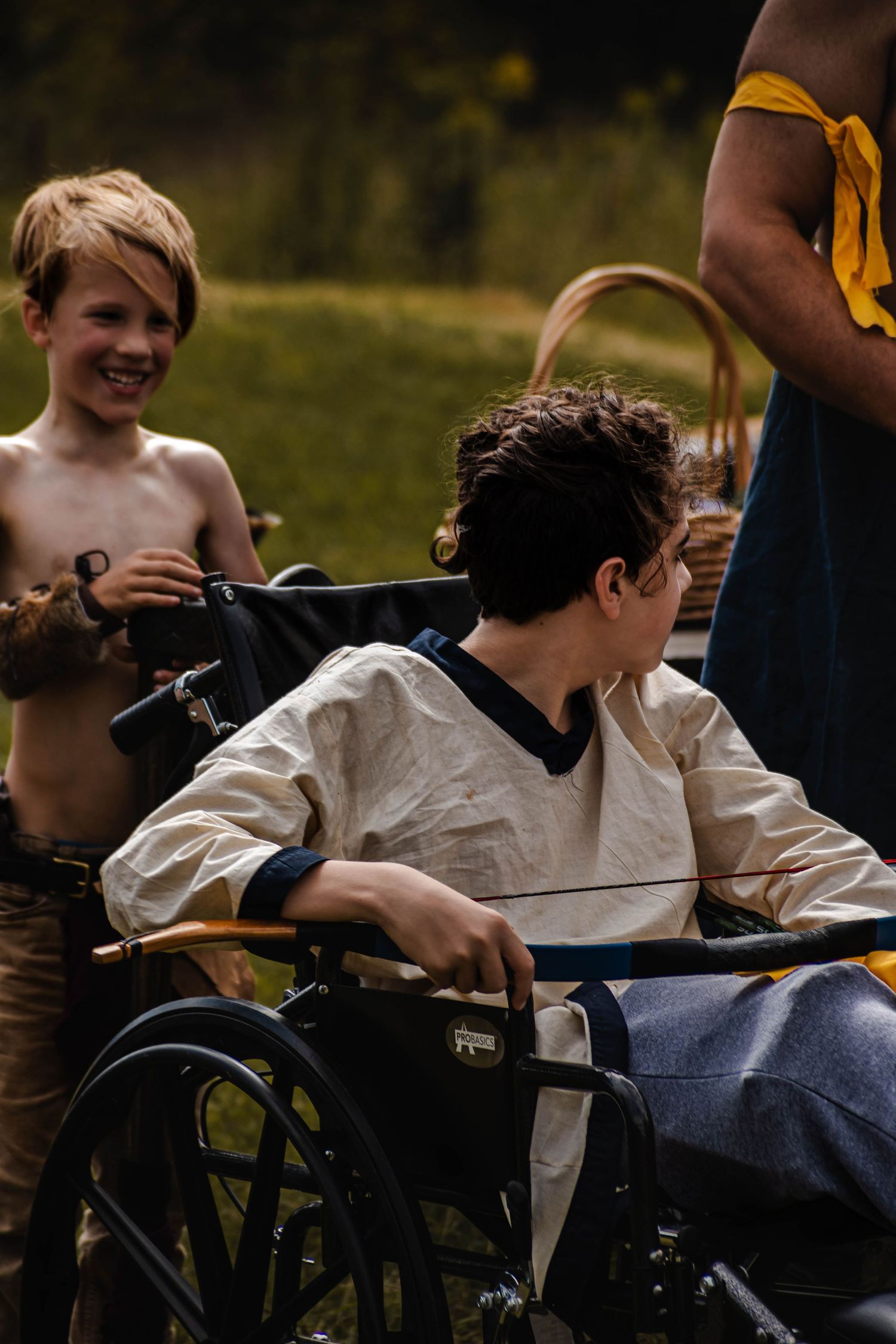 A person in a wheelchair outdoors with others during what appears to be a summer gathering.