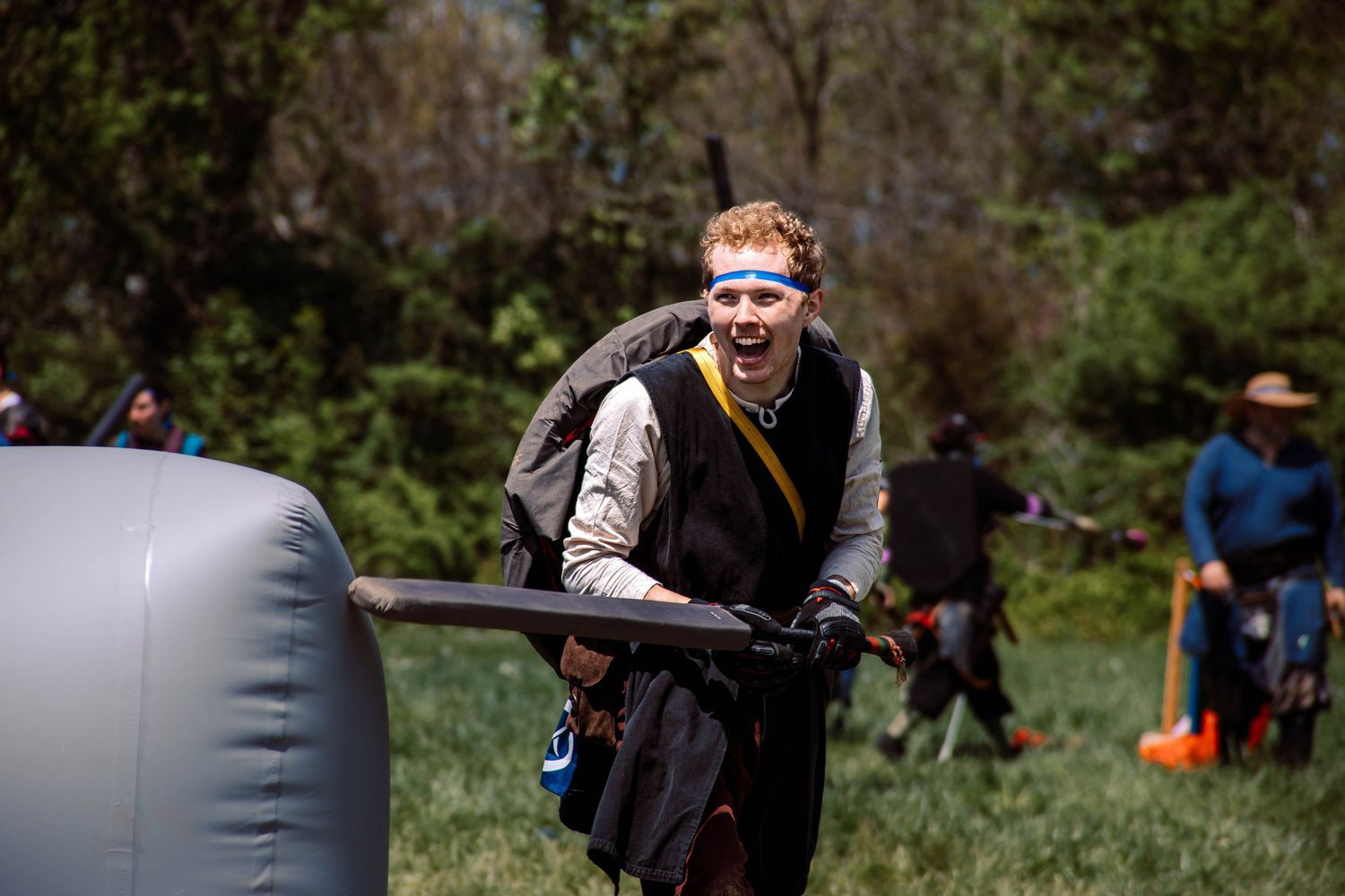 A group of people participate in outdoor archery practice with bows and arrows at a wooded range.