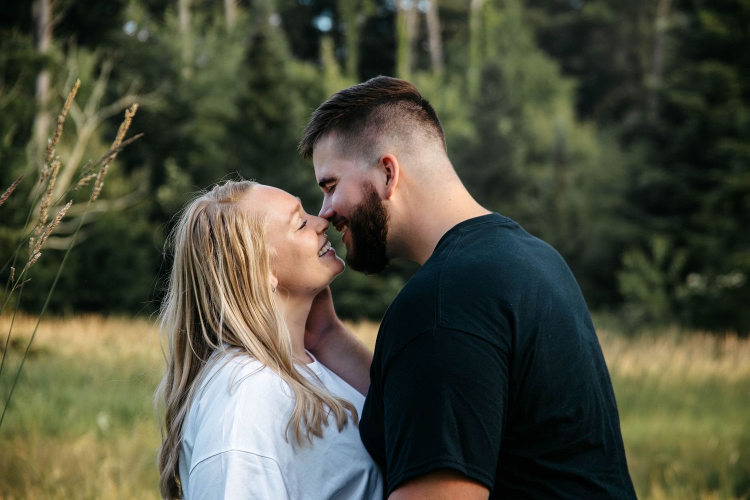 A romantic couple shares tender moments together in a sunlit outdoor field with trees in the background.