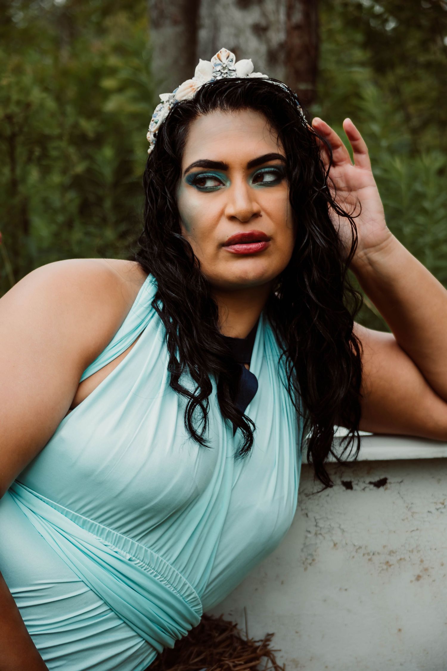 Glamour portraits in a mint green dress with dramatic makeup against trees.