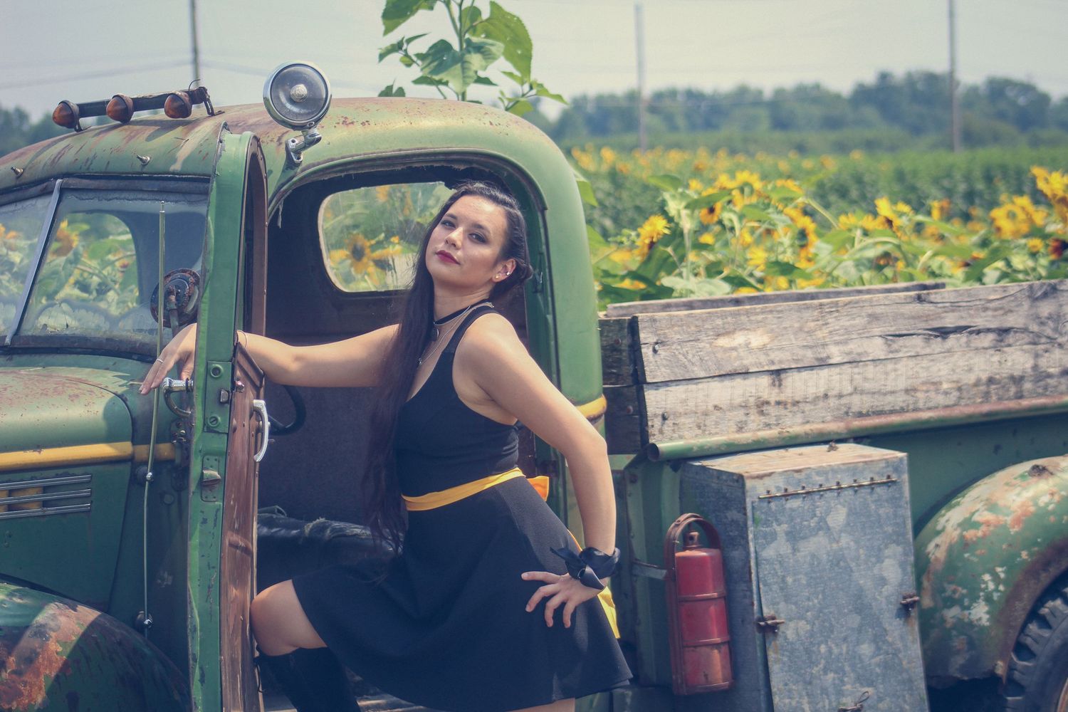 A vintage green farm truck parked near a blooming sunflower field on a summer day.