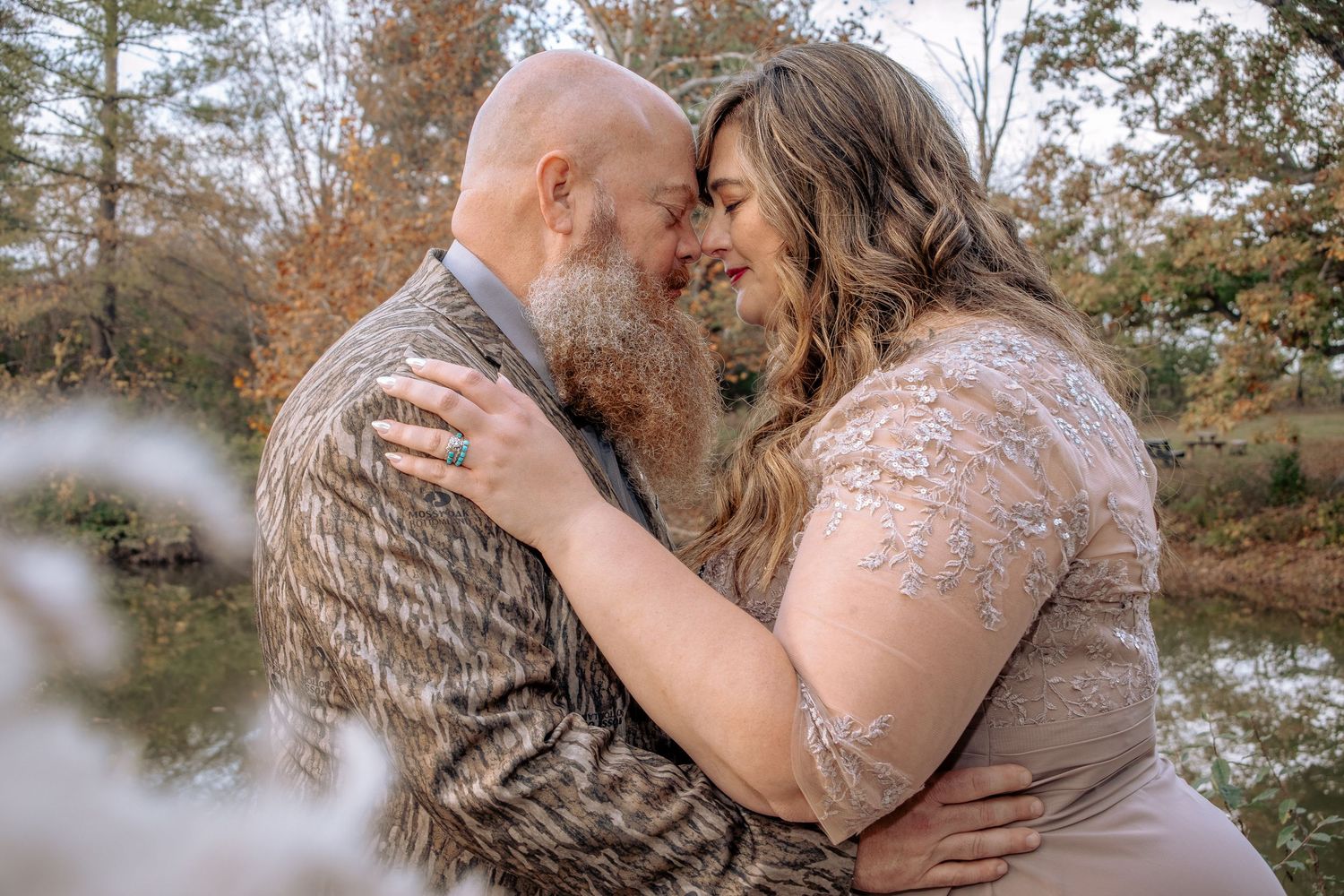 A couple embraces in a romantic kiss surrounded by autumn trees and falling leaves during their outdoor photoshoot.