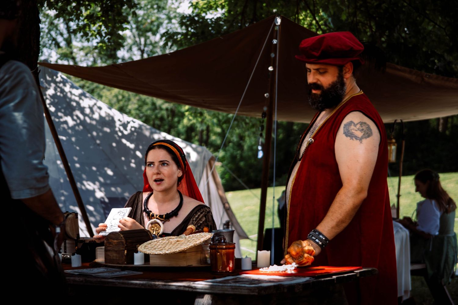 Two people working at an outdoor food vendor booth with a brown canopy on a sunny day.