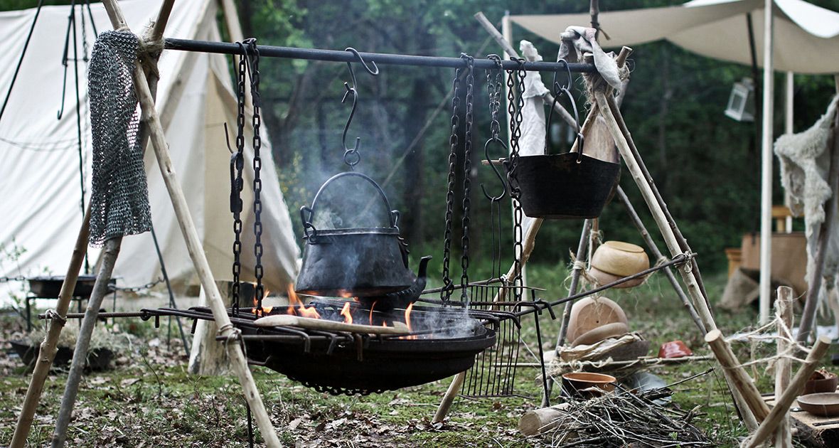 A row of outdoor grills and smokers at a barbecue event with smoke rising from multiple cooking stations.