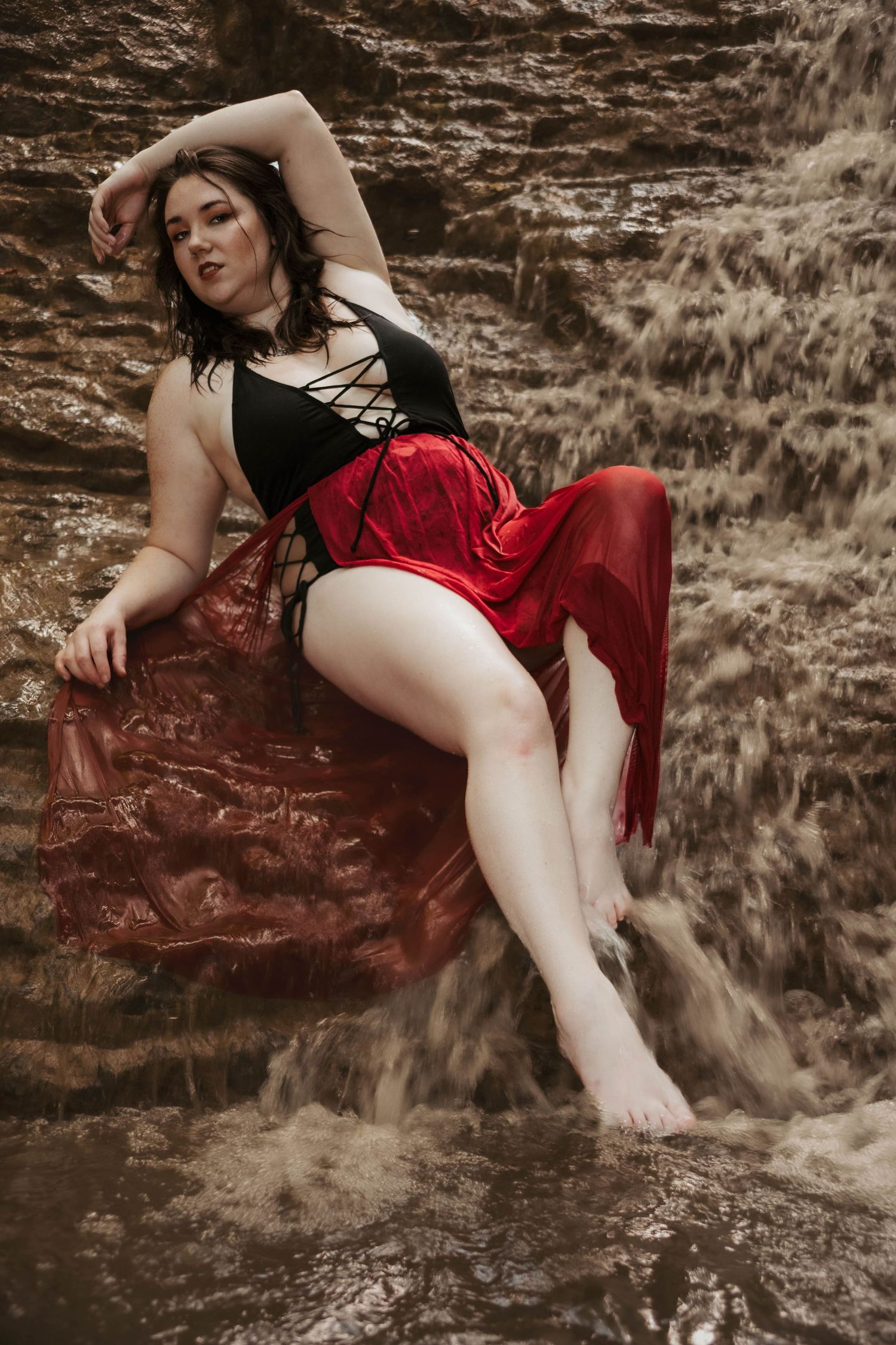 Artistic boudoir photo by waterfall with flowing red skirt and black top.