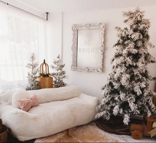 Cozy bedroom corner decorated for winter with a flocked Christmas tree and white bedding against neutral walls.