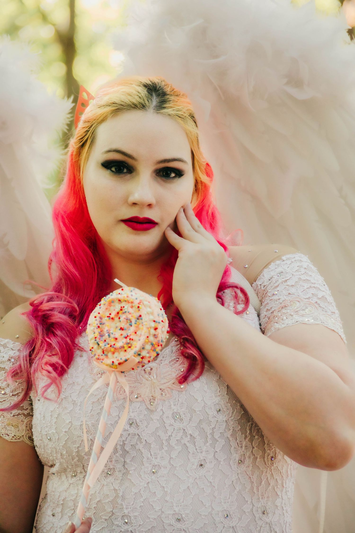A dreamy portrait featuring vibrant pink hair, white lace dress, and a decorative lollipop accessory in soft lighting.