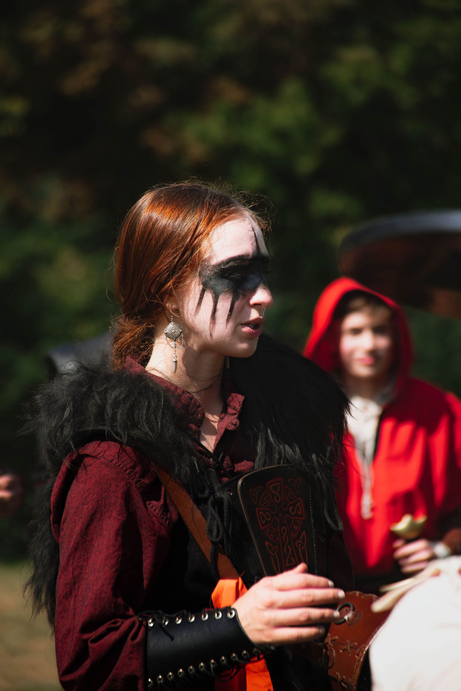 A person in a burgundy medieval costume performs at an outdoor renaissance fair event.