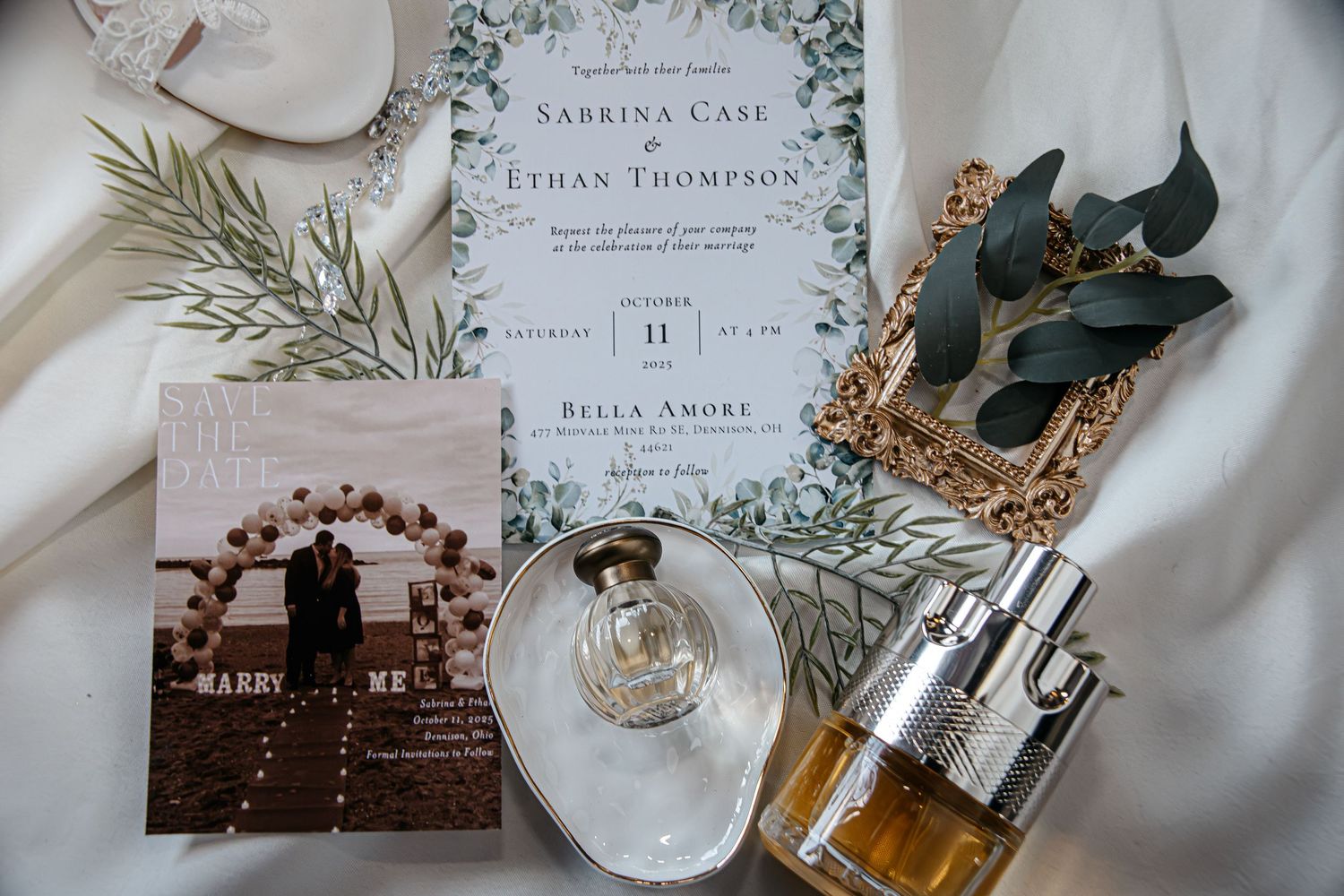 Elegant wedding invitation suite with floral details and calligraphy displayed alongside perfume bottles and decor.