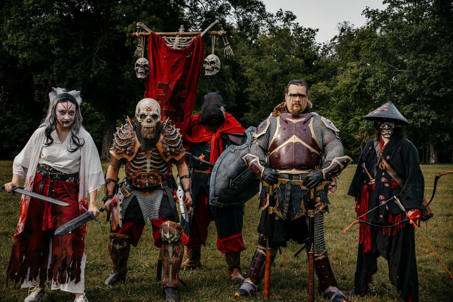 Five people in elaborate fantasy costumes with skeleton and warrior makeup pose outdoors at a medieval LARP event.