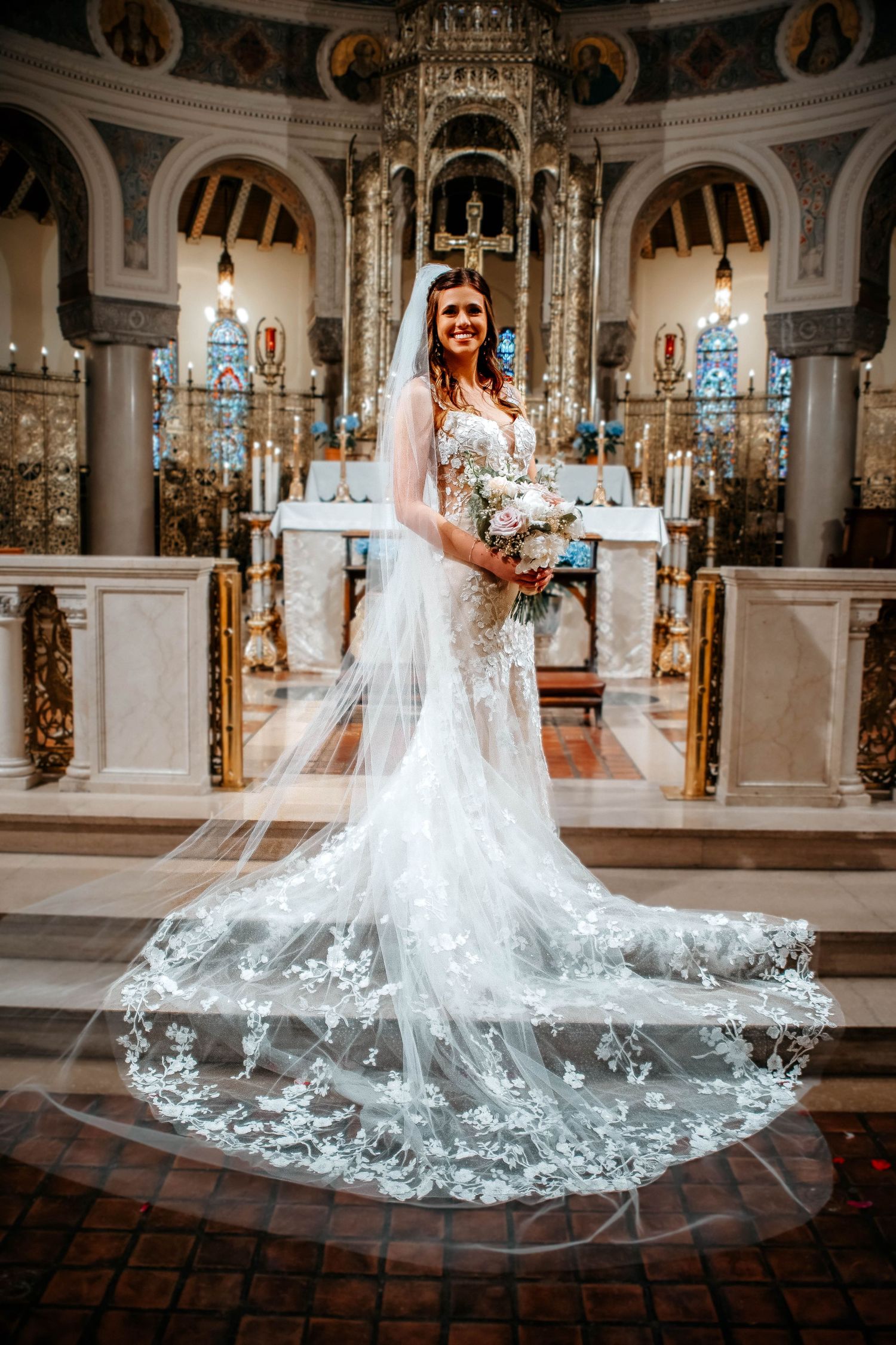 A stunning lace wedding dress with cathedral length veil photographed in an ornate church with elegant chandeliers.