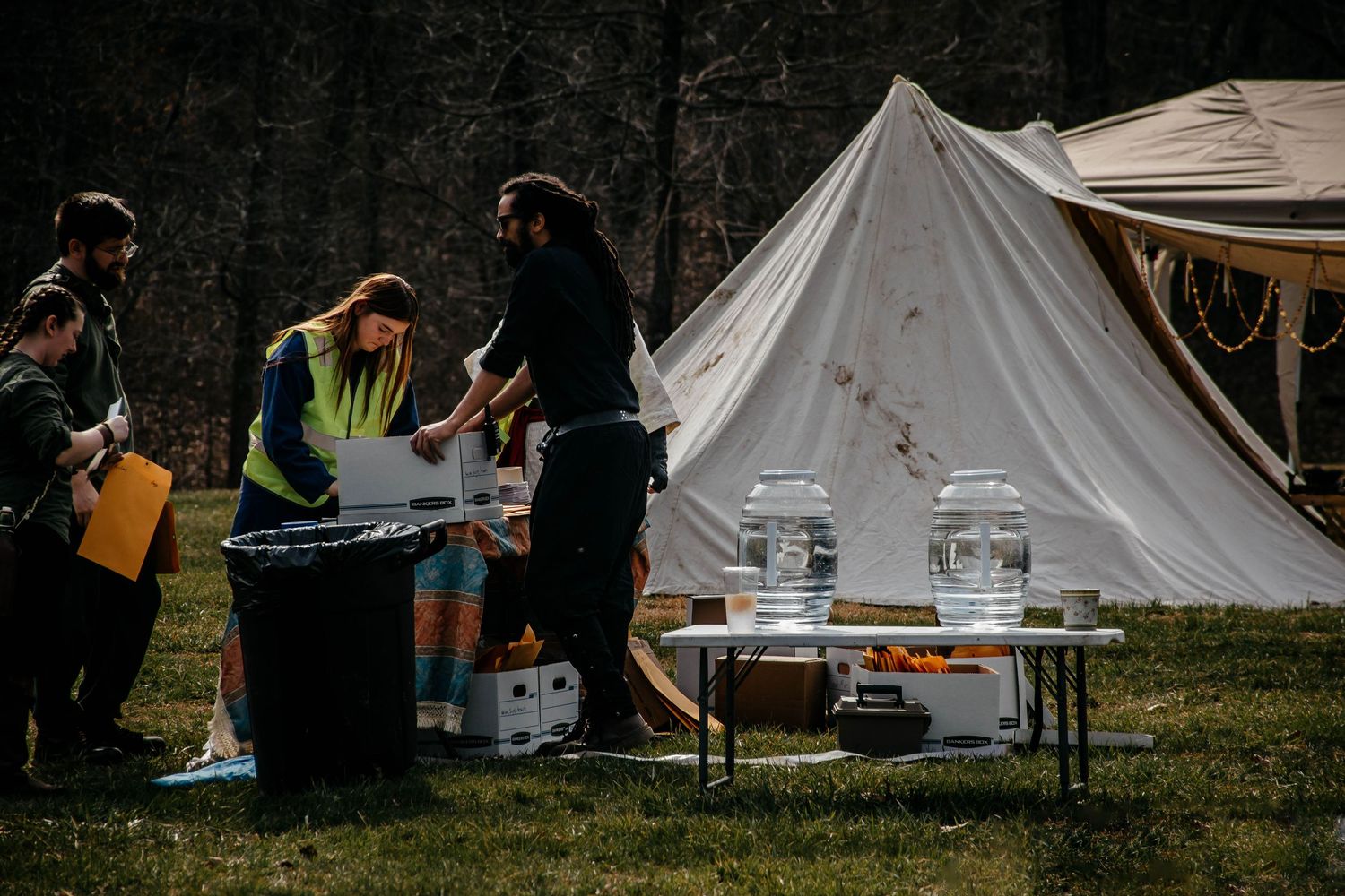 A row of white canvas tents set up in a grassy field with people gathered around for a camping event.