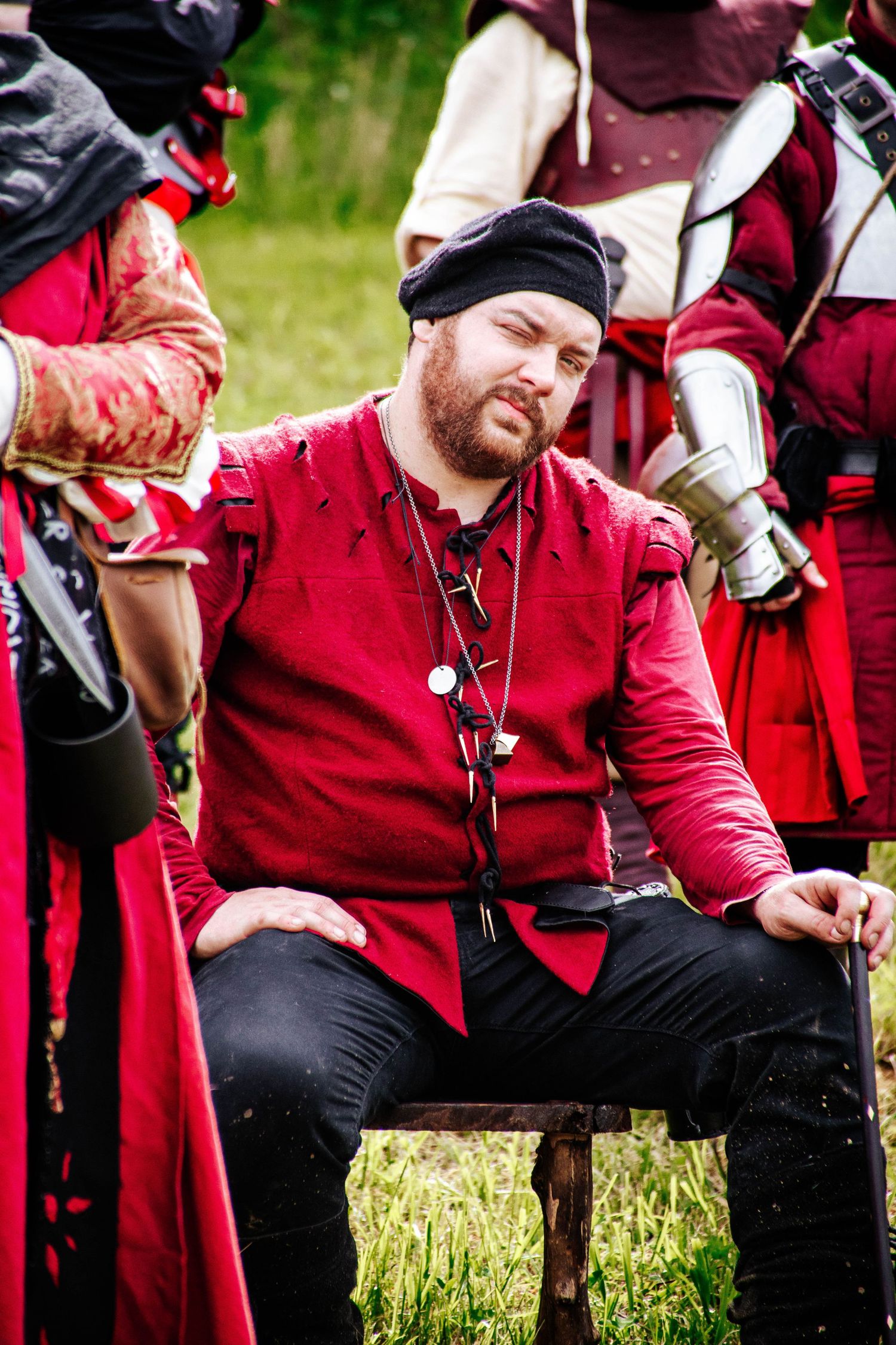 Group of historical reenactors in red coats and period costumes resting on grass during an outdoor event.