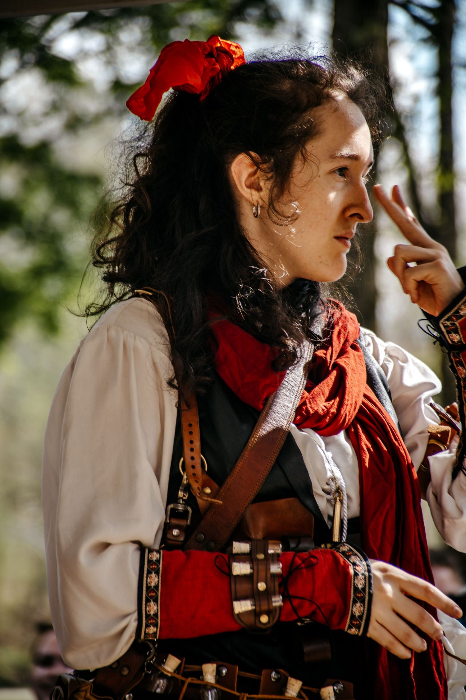 Woman in Renaissance faire costume with red scarf and leather harness, posing outdoors in period attire.