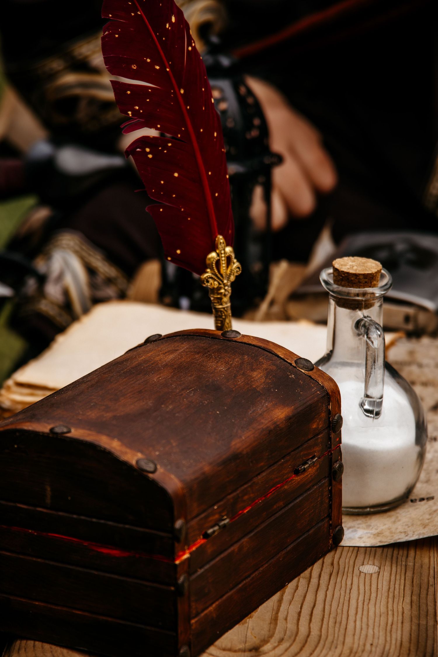 Vintage wooden chest with red quill pen and glass bottle on rustic table.