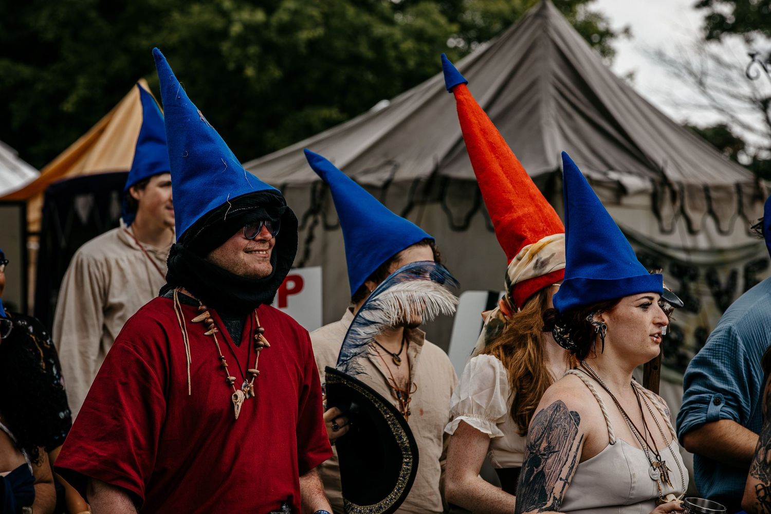 People wearing colorful medieval pointed hats at a Renaissance faire with tents in the background.