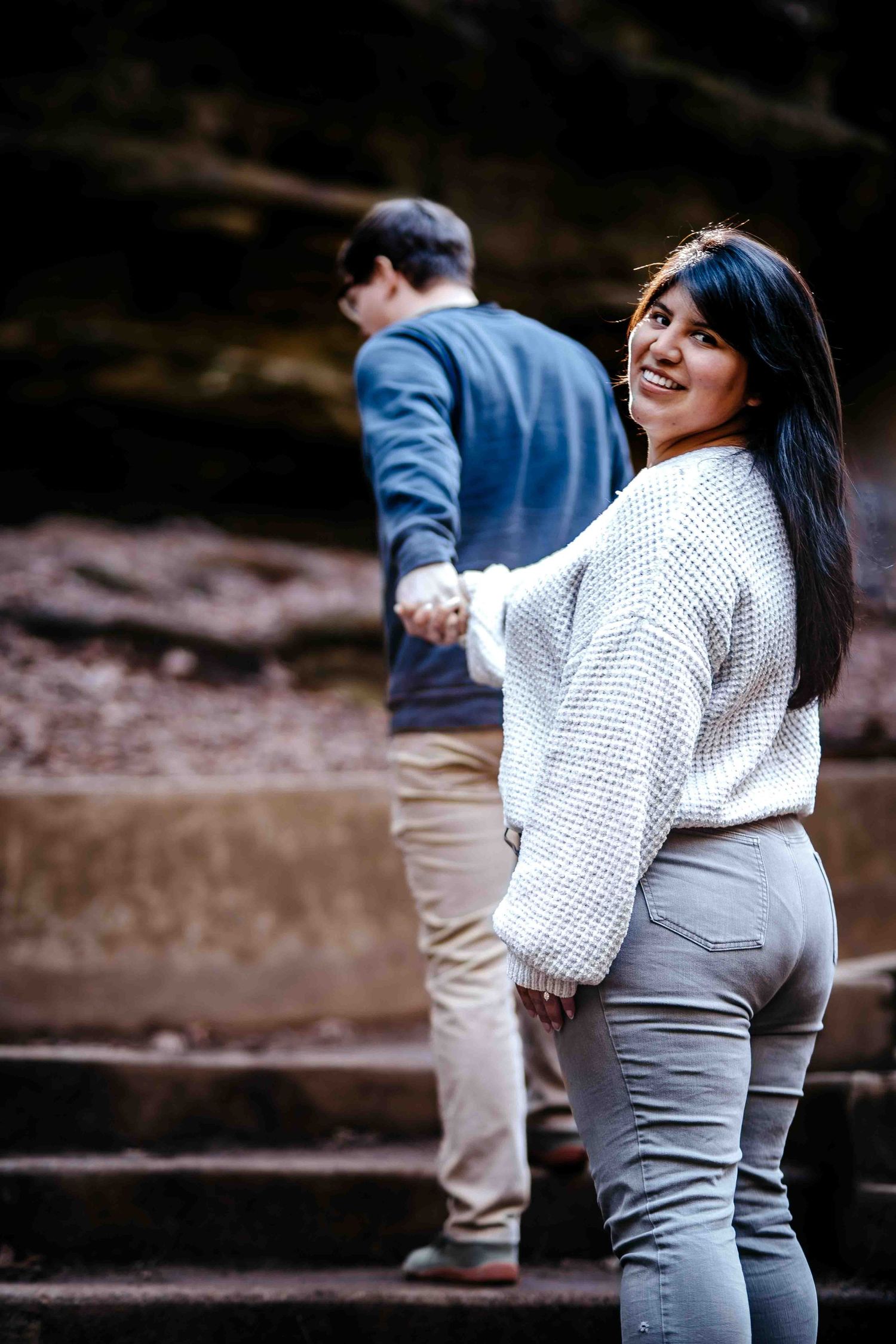A couple in casual attire poses together on stone steps during an outdoor photoshoot.