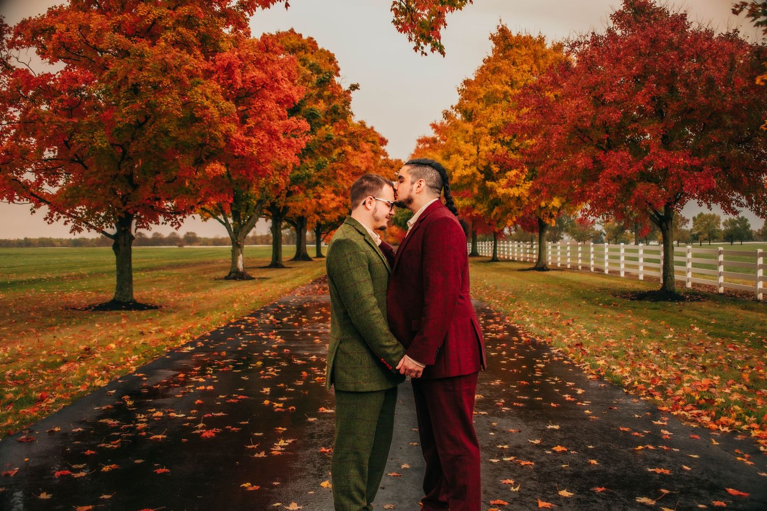 Autumn trees with vibrant red and orange foliage create a romantic backdrop for a couple's outdoor photoshoot.