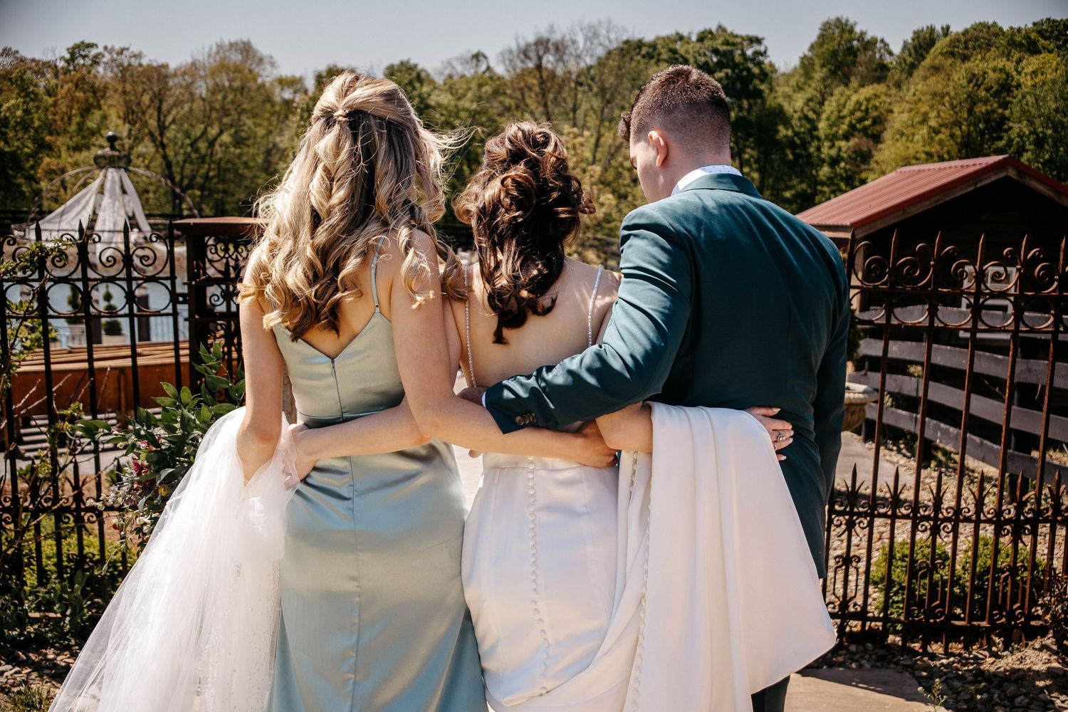 A wedding couple walks hand in hand through a garden path next to an ornate metal fence on their special day.